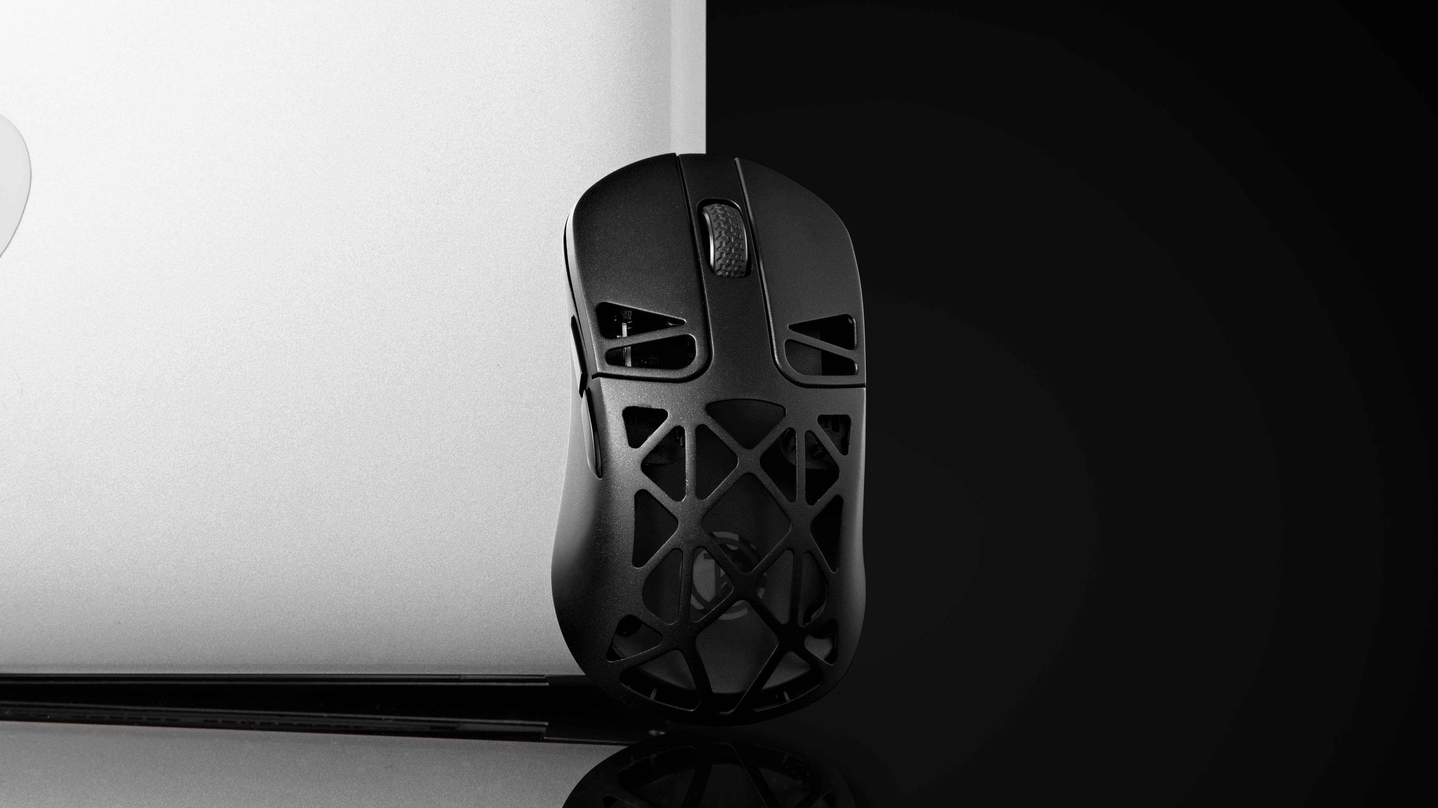 Czarna mysz gamingowa z otwartym designem obok laptopa.