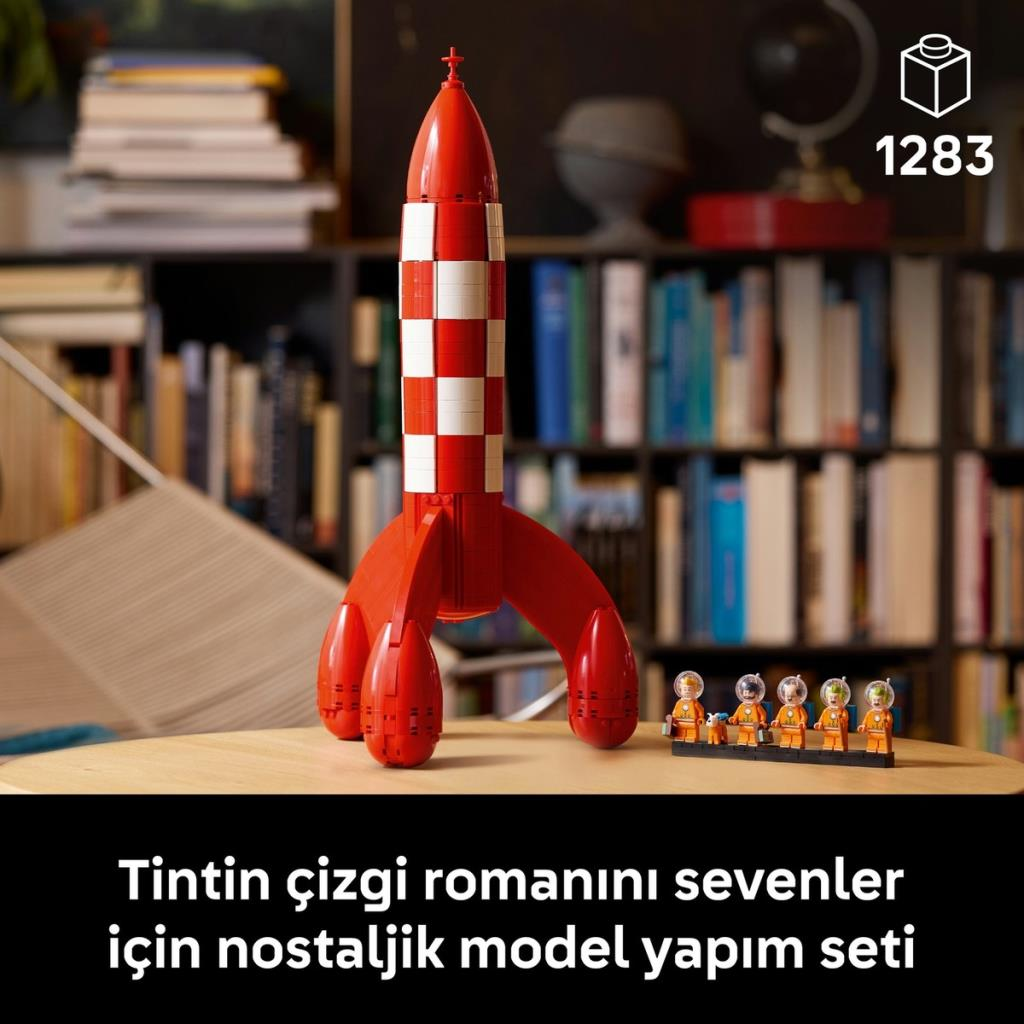 Önde beyaz kareli kırmızı Lego roket modeli ve küçük figürler, arkada kitaplıklar.