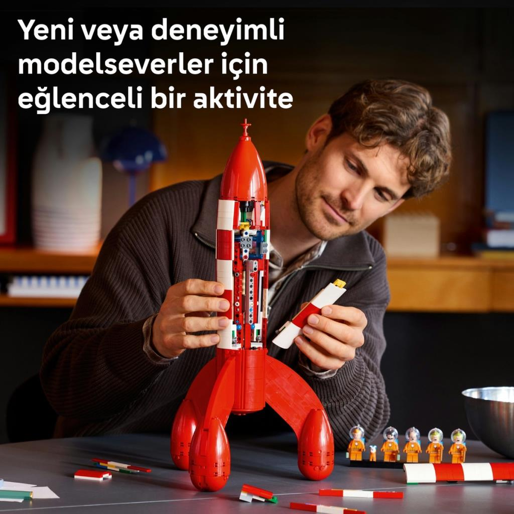 Bir adam kırmızı LEGO roket inşa ediyor. Yanında birkaç küçük figür duruyor.