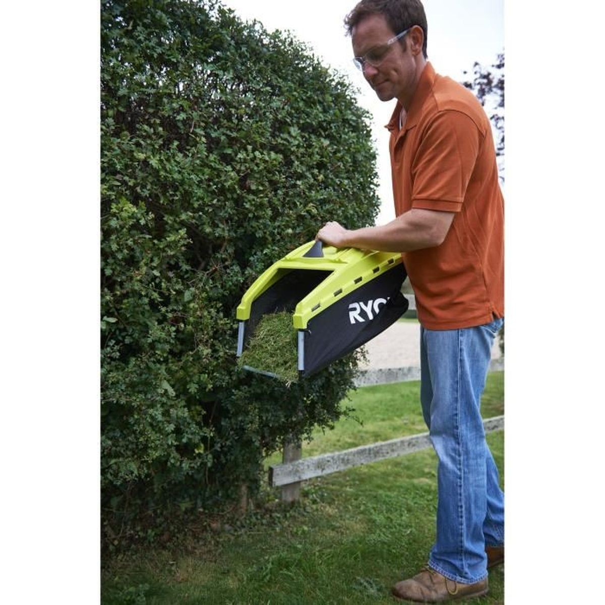 Hombre usando un accesorio amarillo para recortar césped en arbusto verde al aire libre.