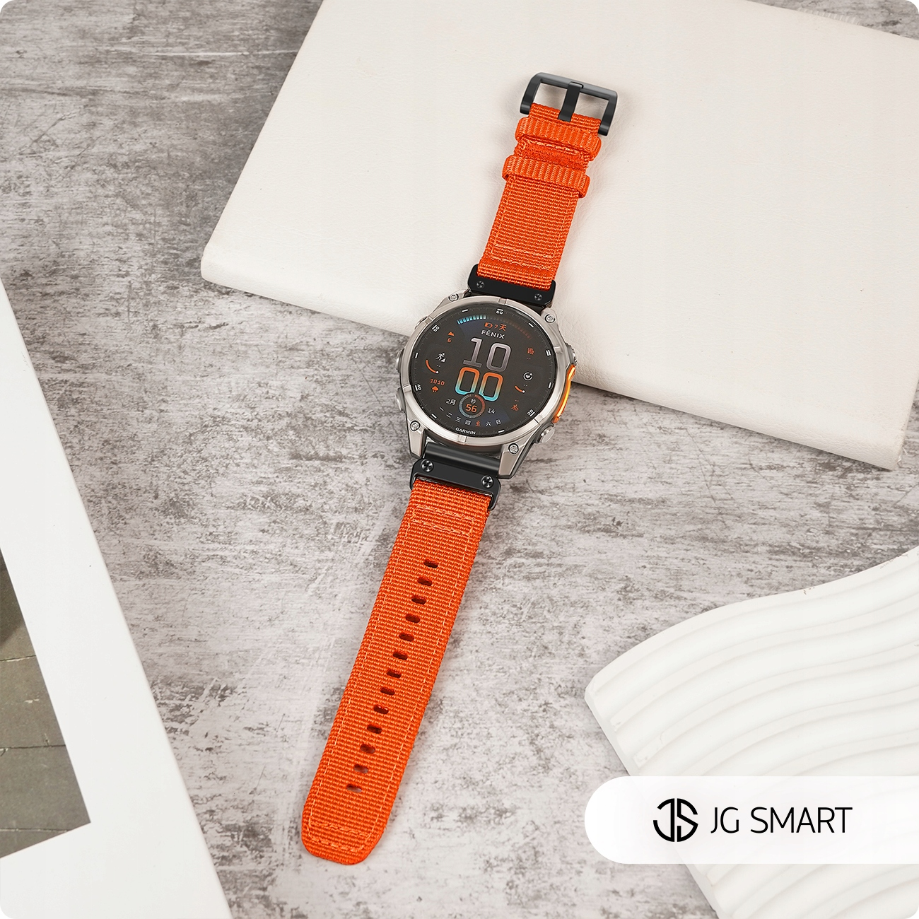 Pomarańczowy smartwatch z czarną tarczą na szarej, teksturowanej powierzchni.