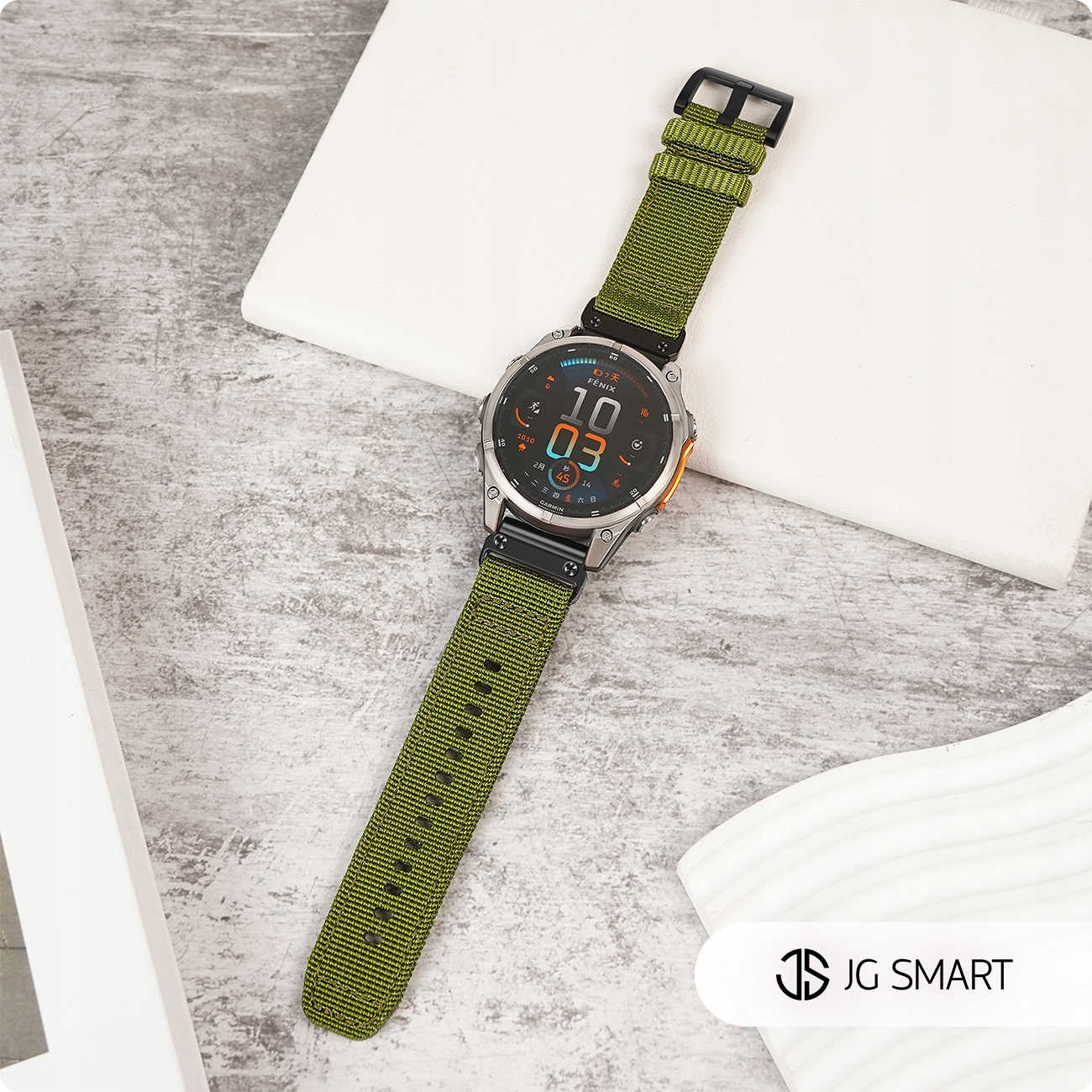 Srebrny smartwatch z zielonym paskiem z tkaniny na szarej powierzchni.