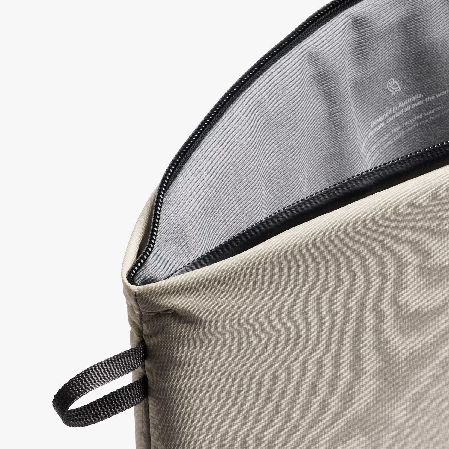 Una pochette in tessuto beige con cerniera nera e manico ad anello nero. Etichetta interna: 'Progettato in Australia'.
