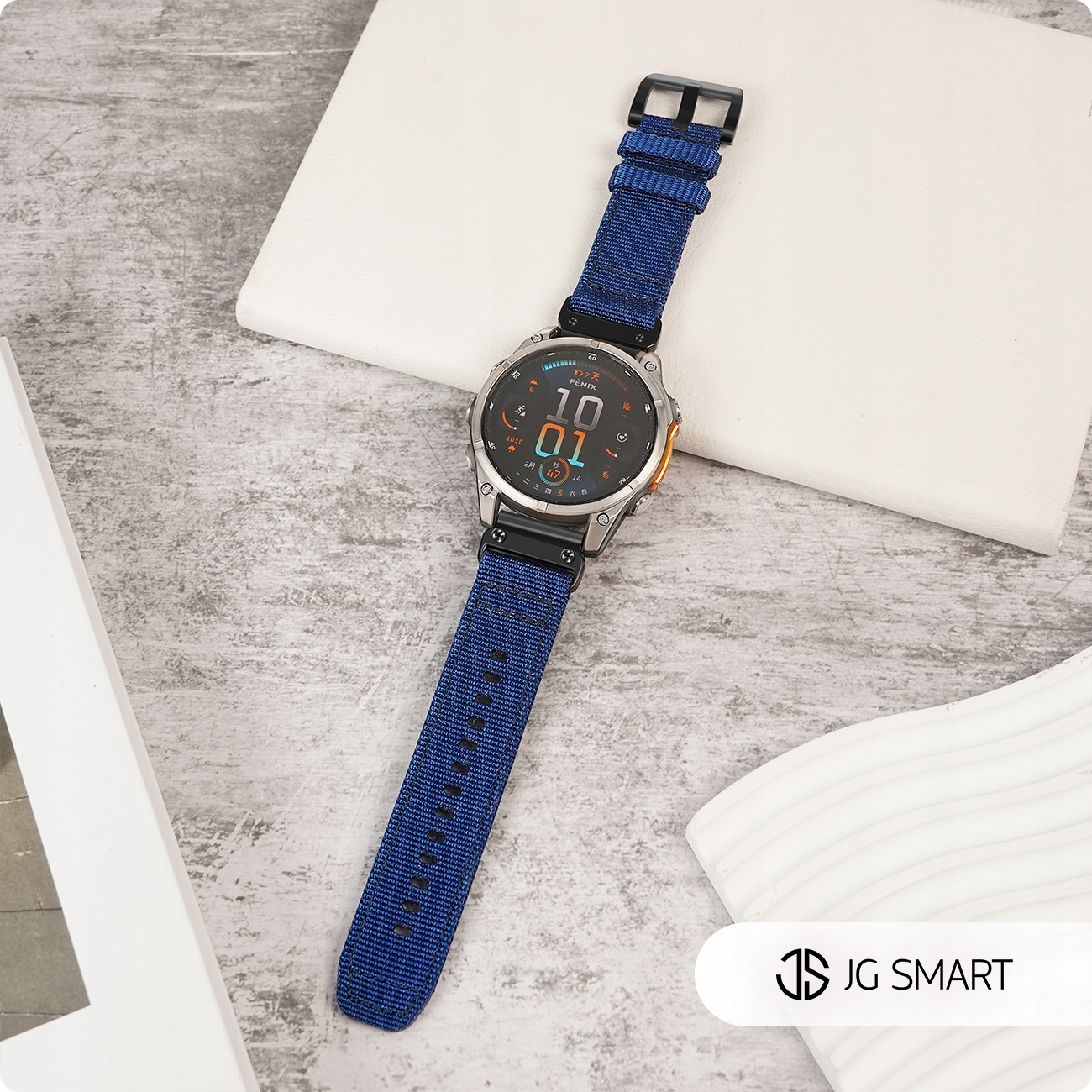 Srebrny smartwatch z niebieską opaską na szarej powierzchni.