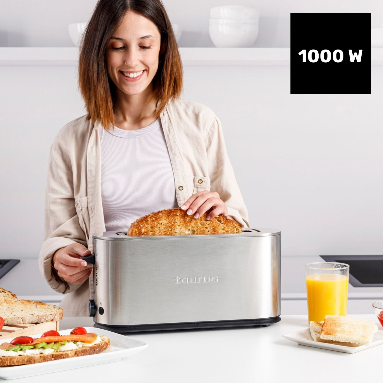 Una mujer saca tostadas de una tostadora plateada. Al lado hay un vaso de zumo.