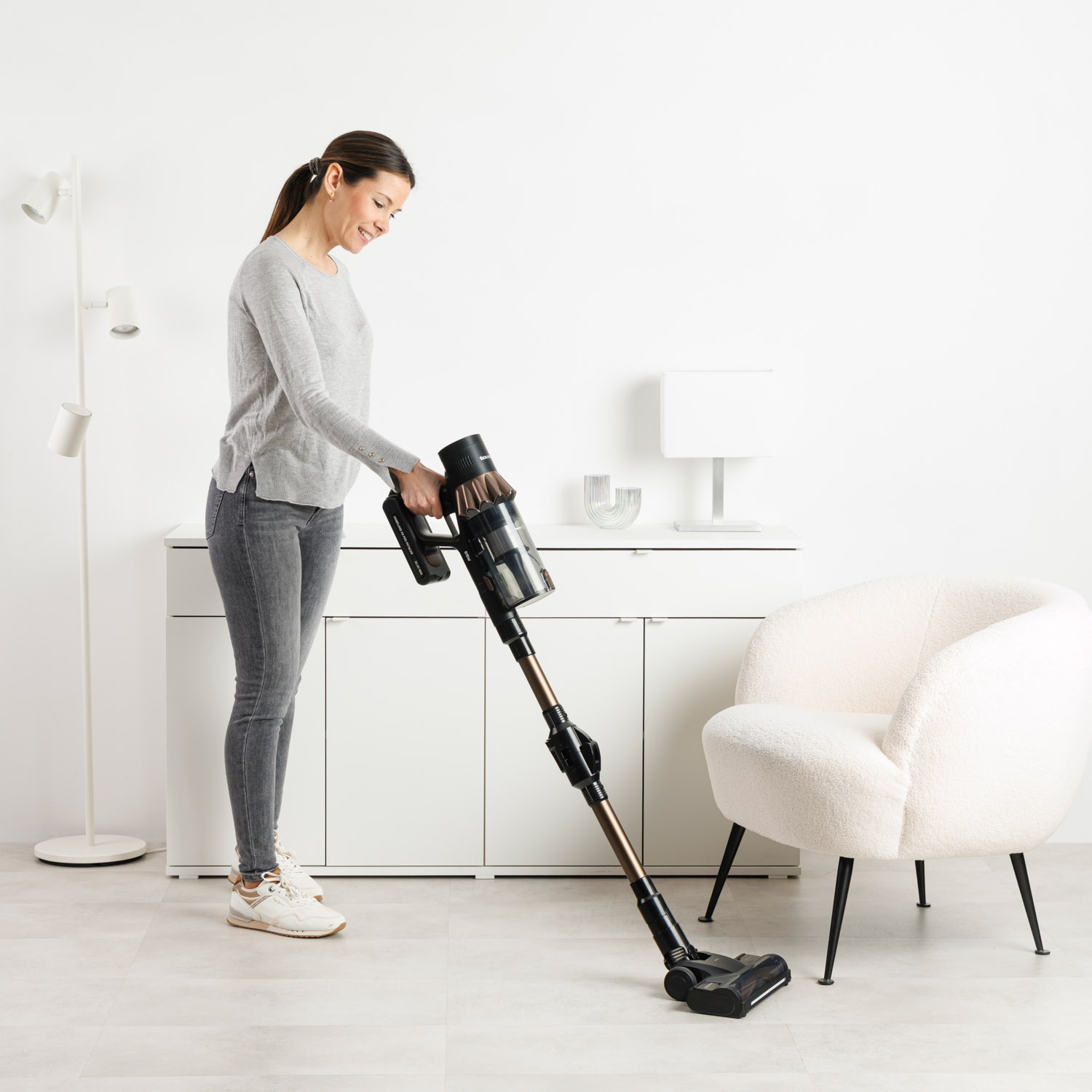 Una mujer aspira una habitación luminosa con una aspiradora inalámbrica.
