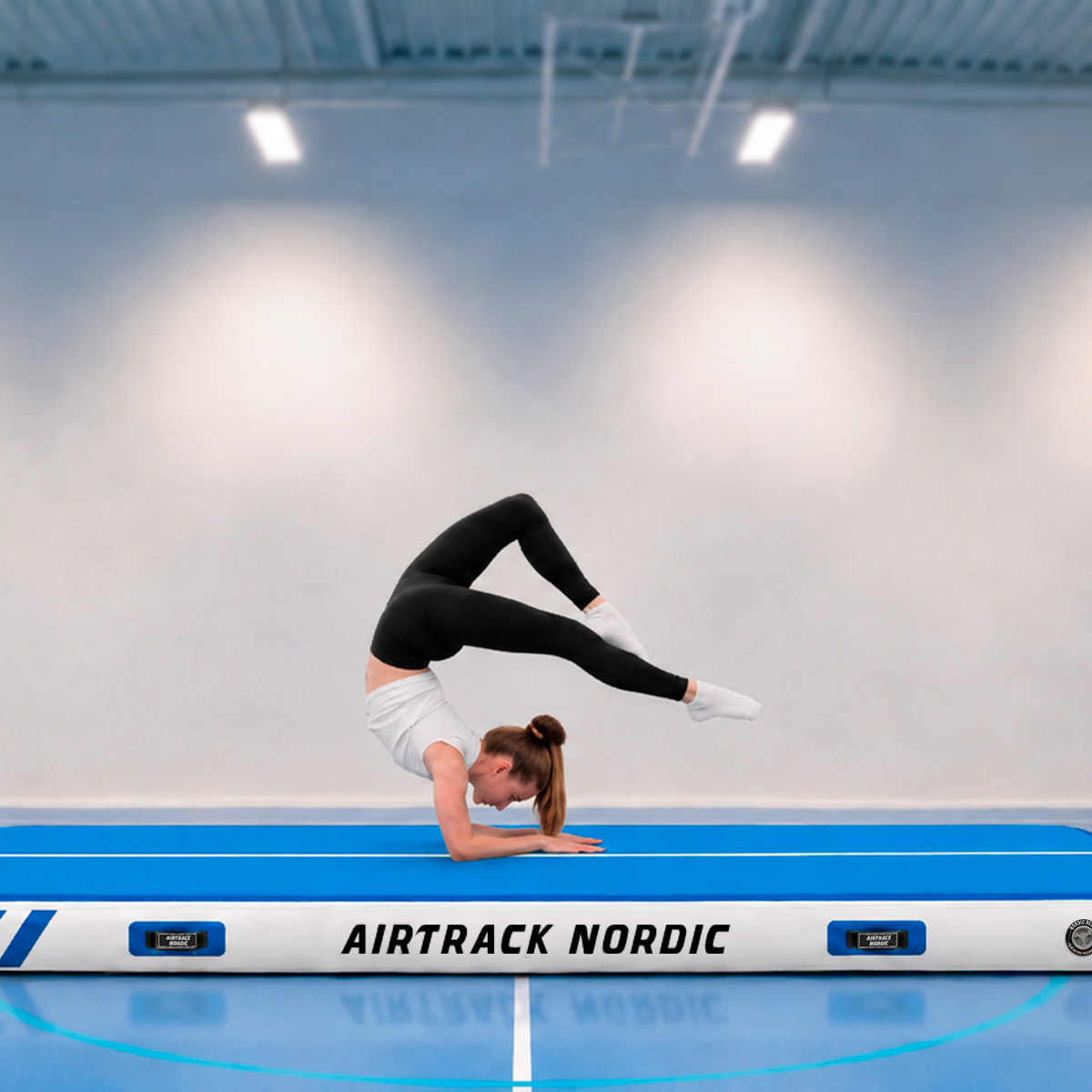Gimnastyczka balansuje na rękach w pozycji mostka na niebieskim airtracku.