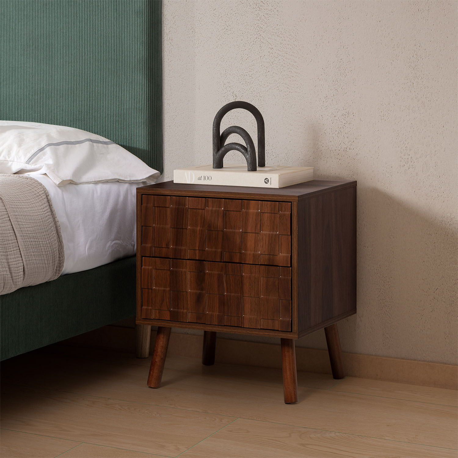 Una mesita de noche de madera oscura con dos cajones junto a una cama verde.