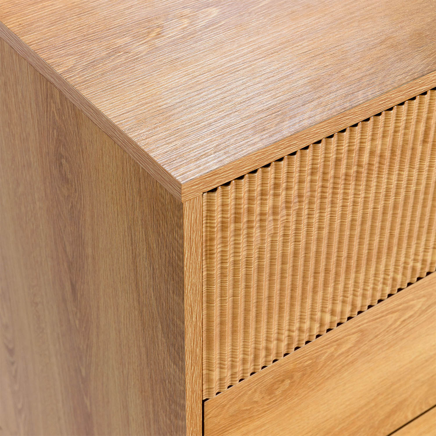 Primer plano de un tocador de madera con frente de cajón acanalado vertical y superficie superior lisa.