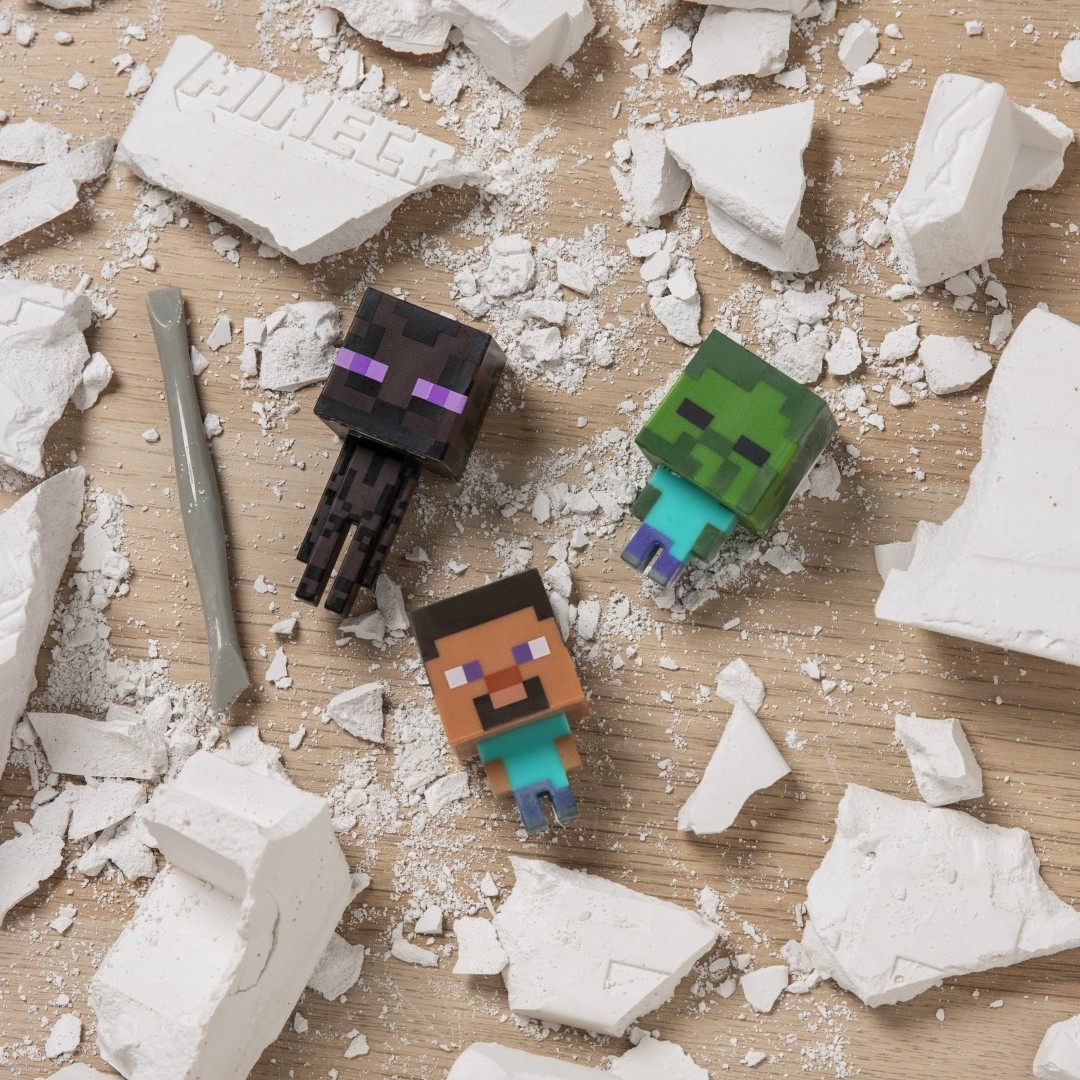 Minecraft-Figuren Steve, Enderman und Zombie liegen verstreut auf Holz mit weißen Bruchstücken.