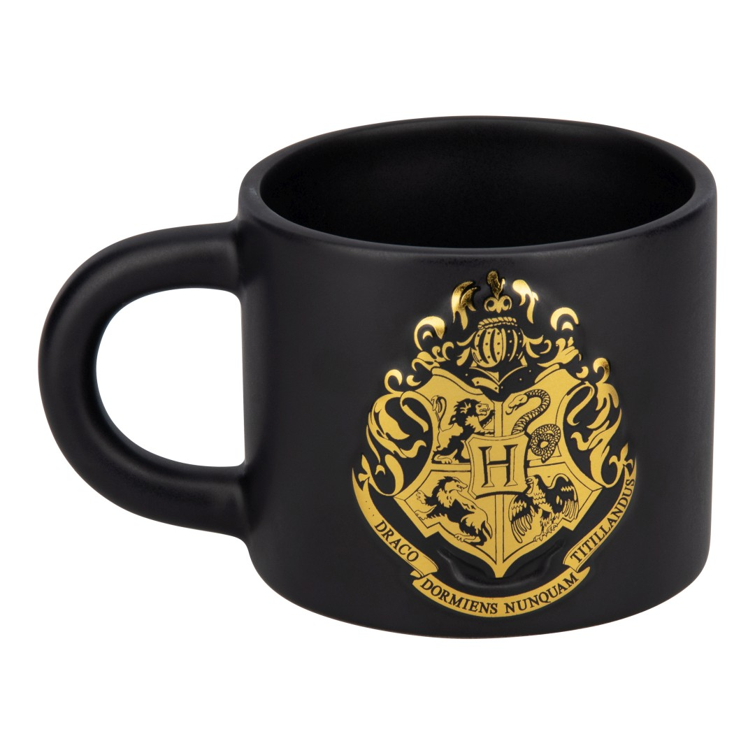 Czarny kubek ze złotym herbem Hogwartu. Herb przedstawia lwa, węża, orła i borsuka.