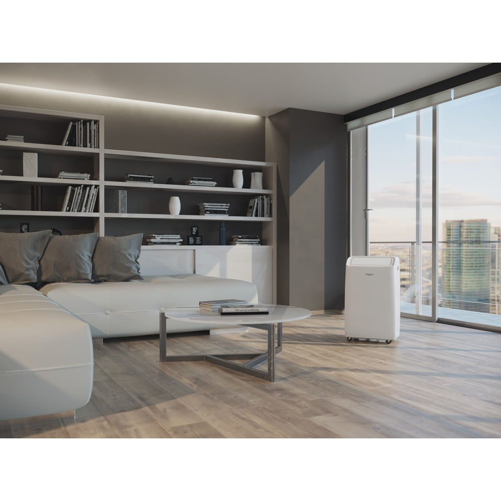 Un enfriador de aire acondicionado portátil blanco se encuentra en una sala de estar moderna con sofá y estanterías.