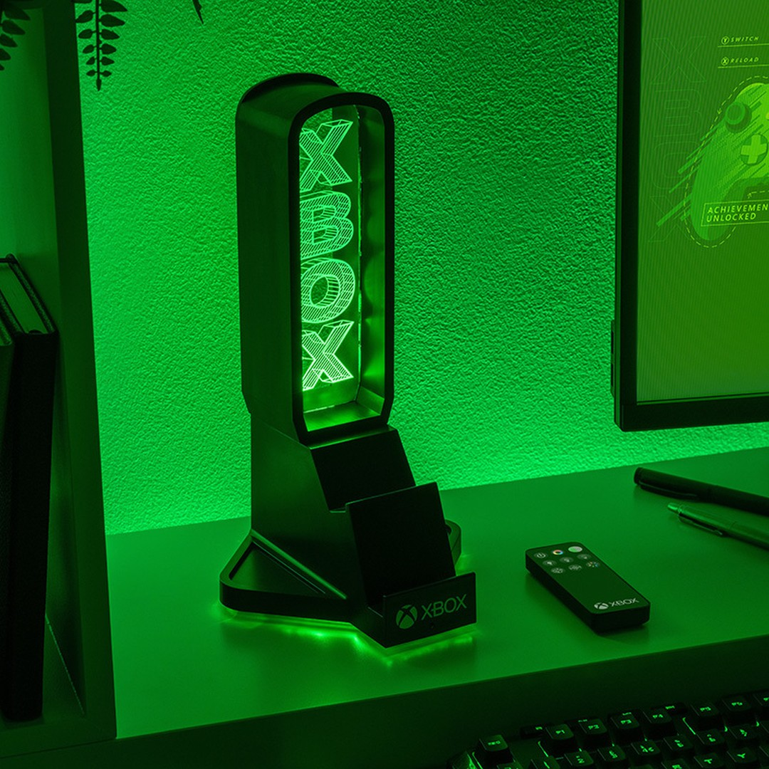 Podświetlany stojak Xbox z logo stoi na biurku obok pilota.