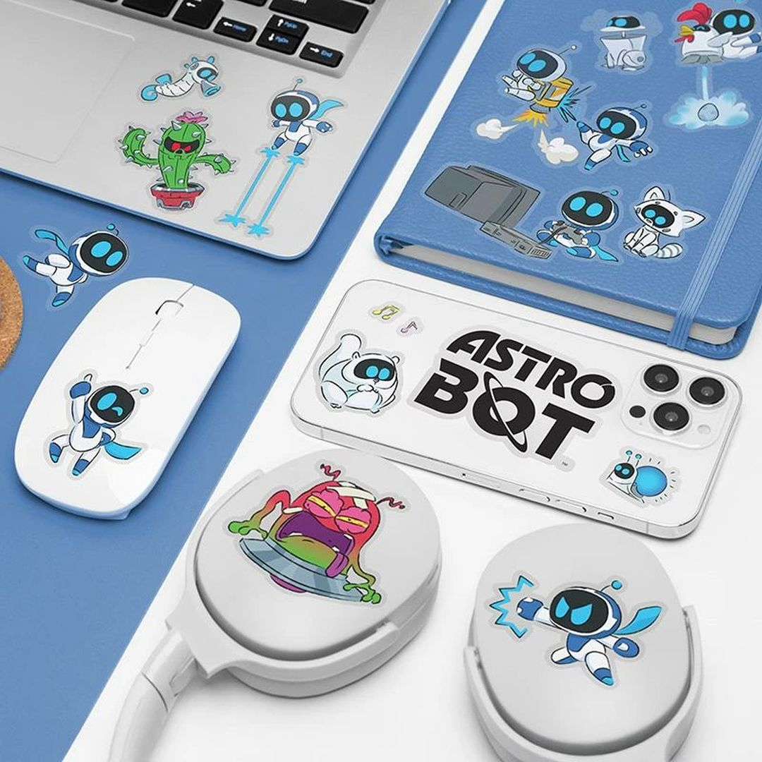 Auf einem Laptop, Maus und Kopfhörern sind Aufkleber mit Astro Bot und anderen Figuren zu sehen.