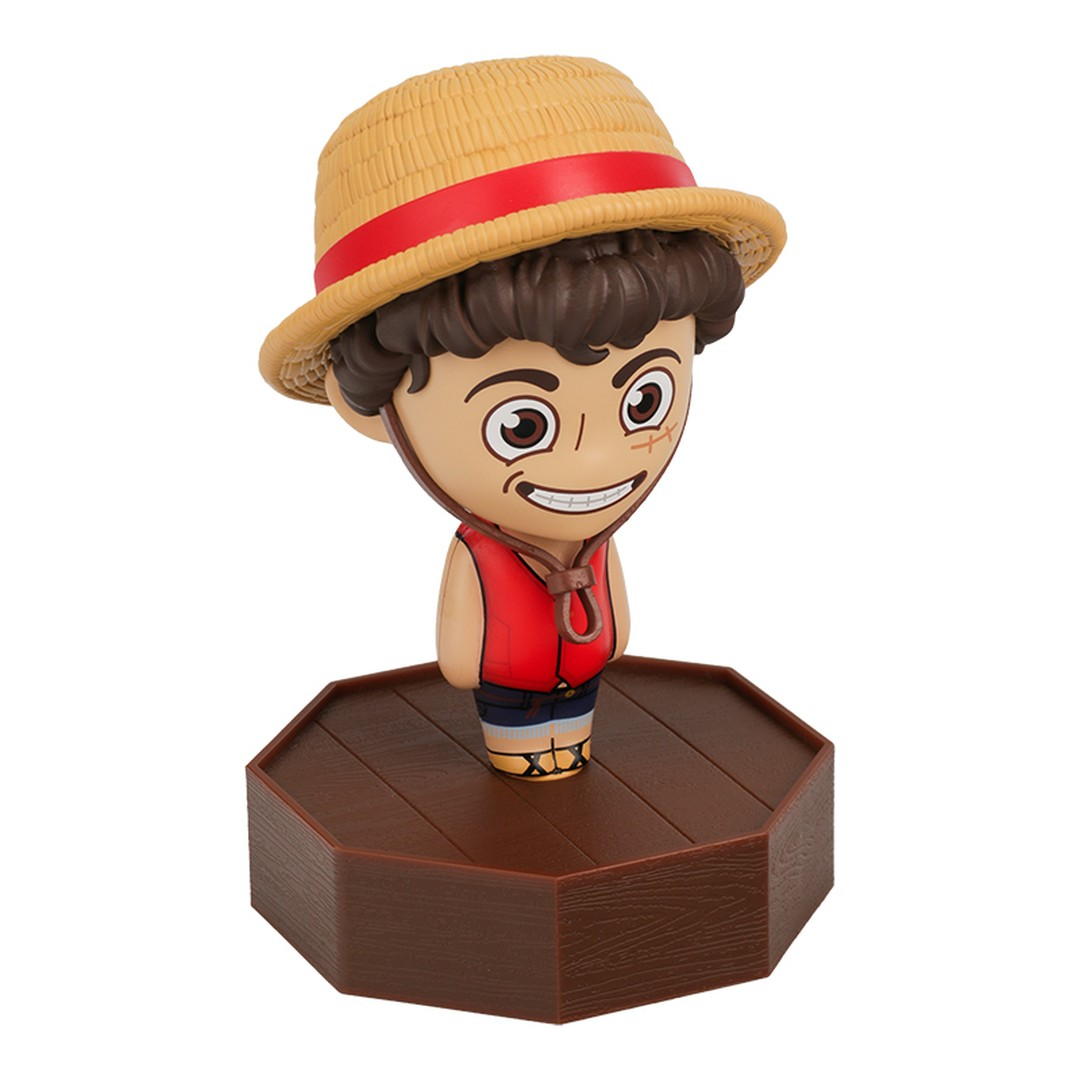 Figurka w stylu chibi ze słomkowym kapeluszem, czerwoną kamizelką i niebieskimi spodenkami na drewnianej podstawie.