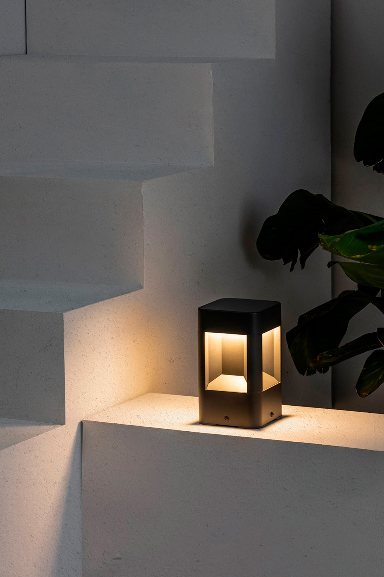 Una moderna lampada nera illumina un gradino di cemento accanto a una pianta.