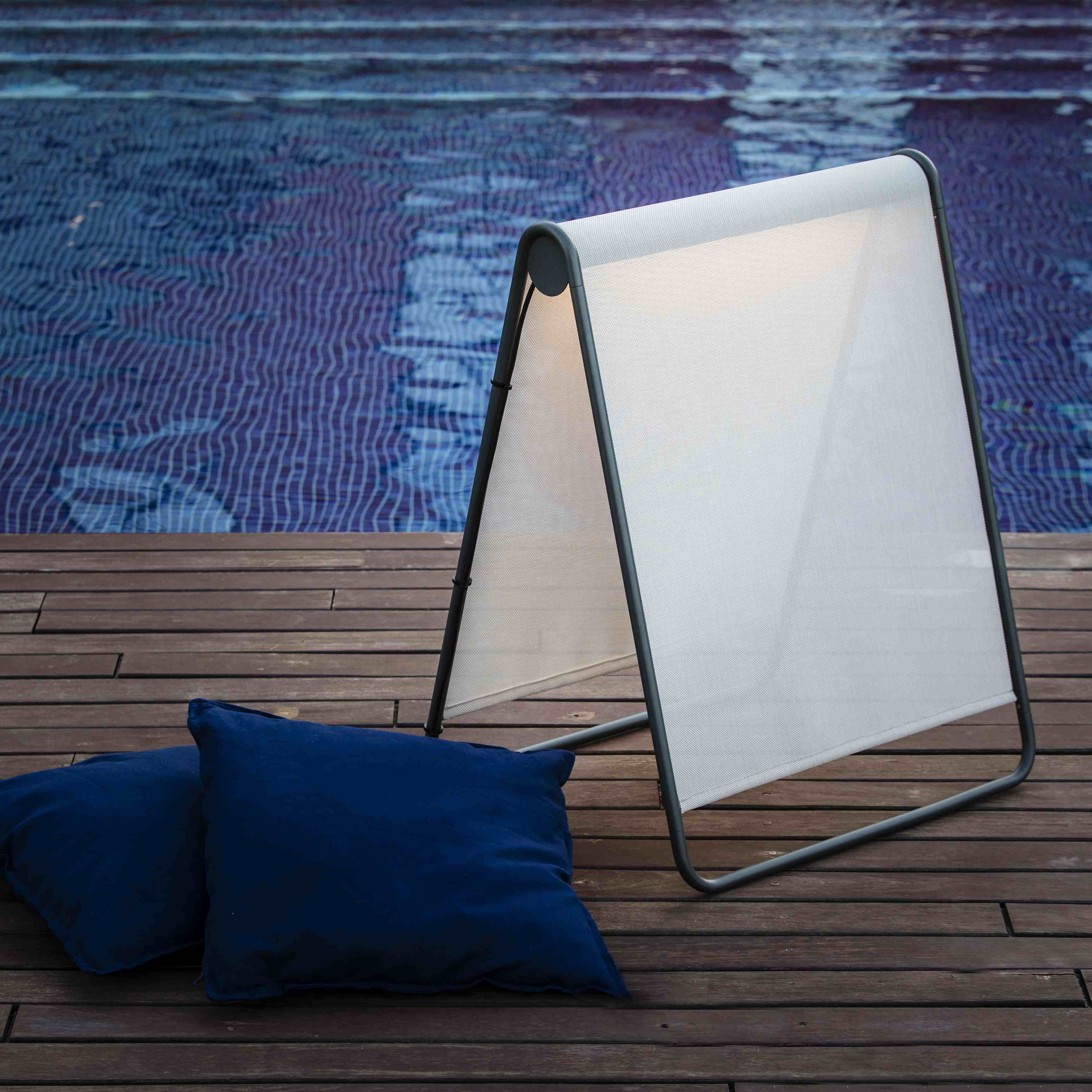 Due cuscini blu riposano su una terrazza di legno accanto a un parasole pieghevole vicino a una piscina.