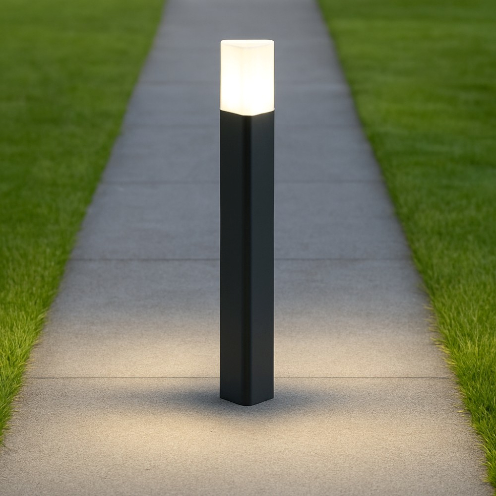 Un bollard scuro illumina un sentiero con erba accanto.