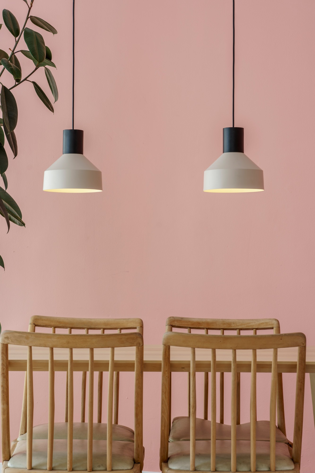 Due sedie di legno a un tavolo davanti a un muro rosa, con pianta a sinistra e due lampade.