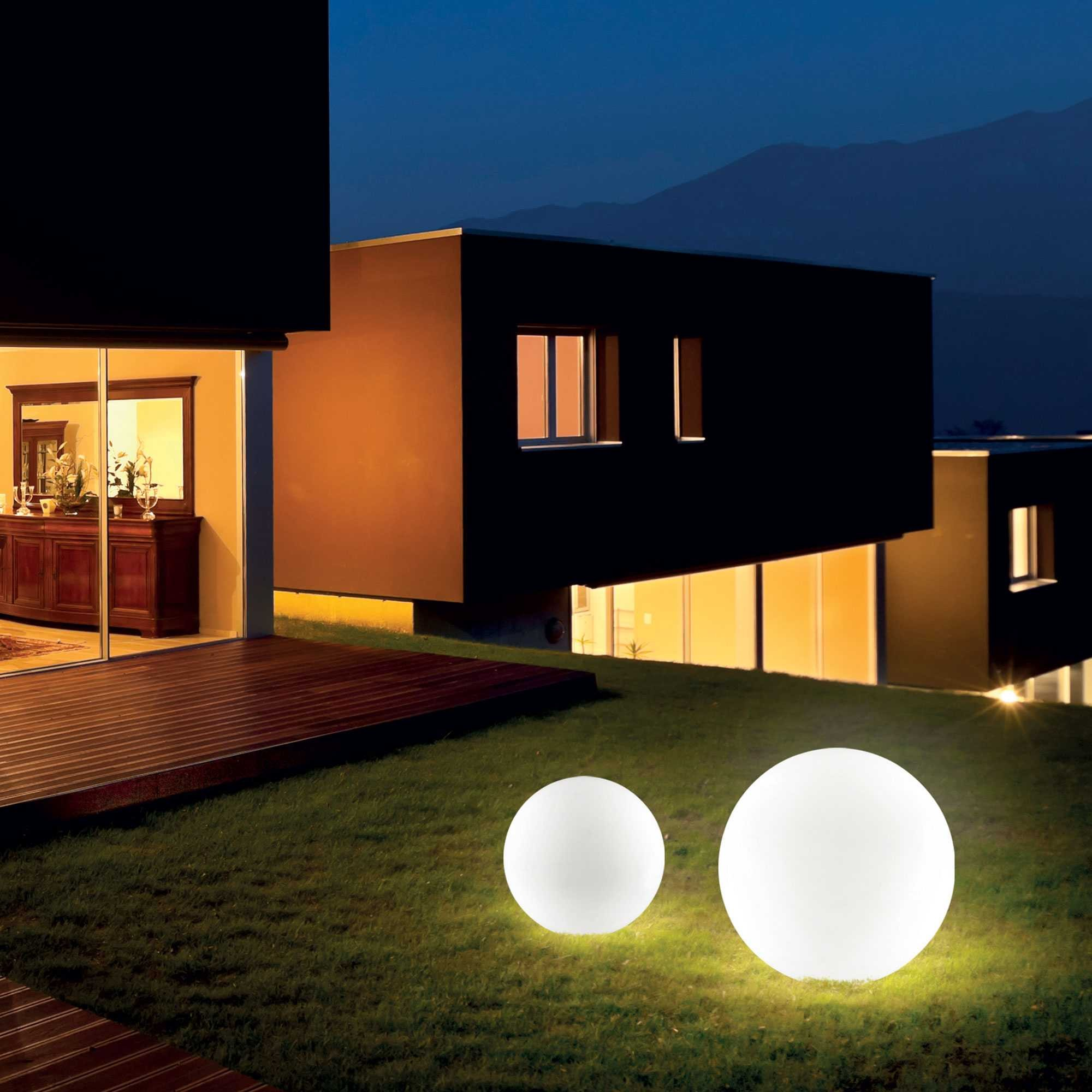 Due sfere luminose su un prato davanti a una casa moderna di notte.