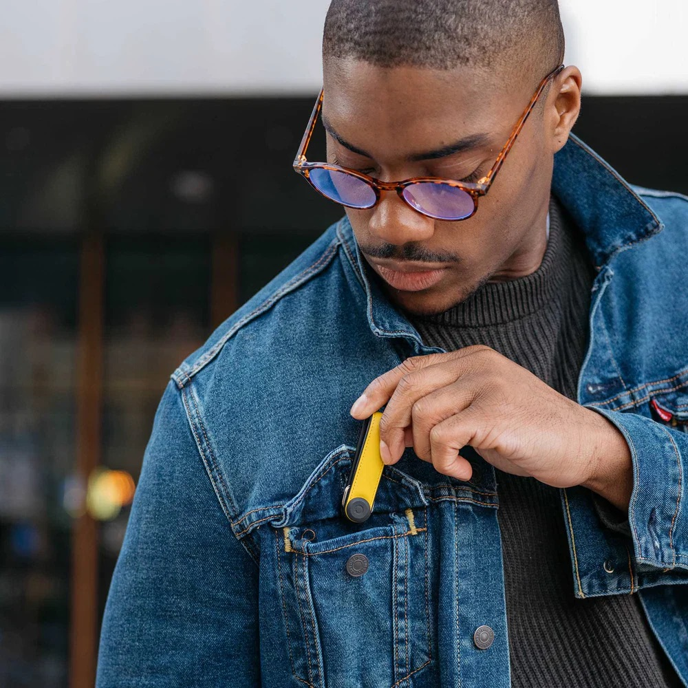 Un uomo con gli occhiali estrae un oggetto giallo dalla tasca della sua giacca di jeans.