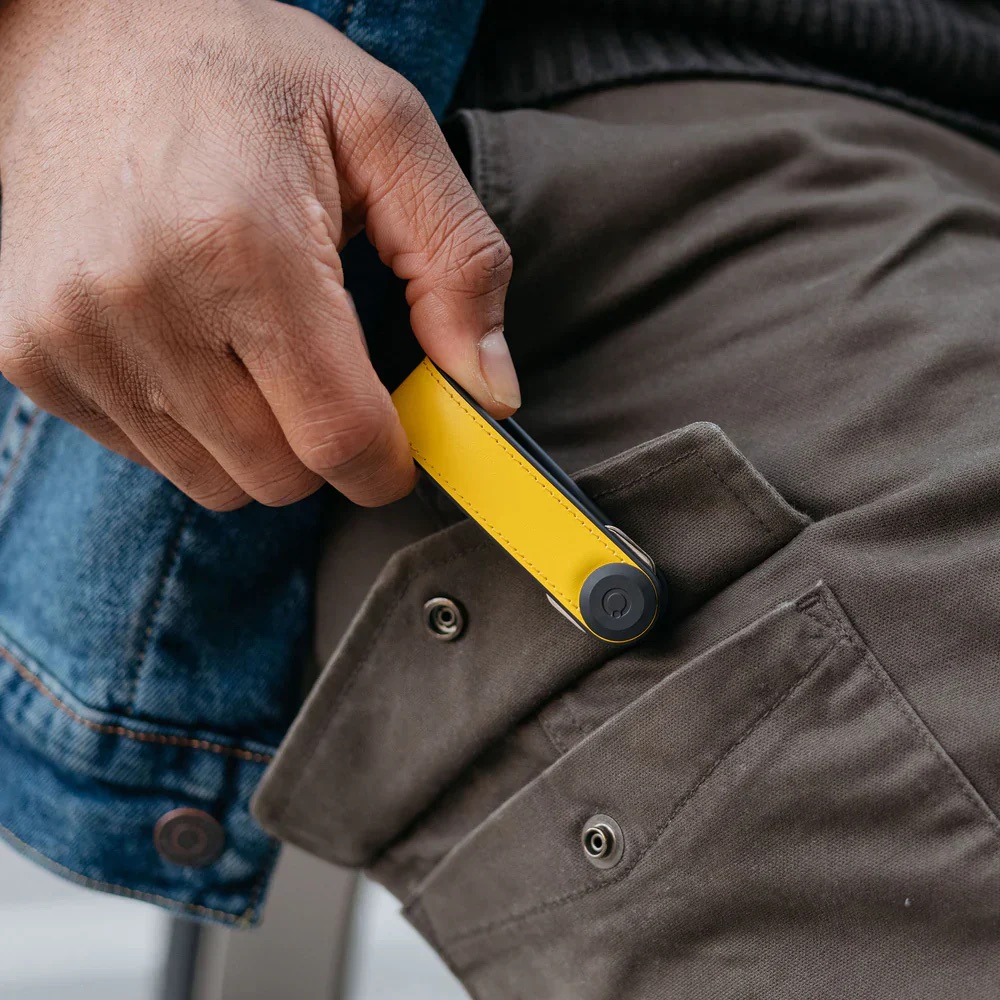 Una mano inserisce un portachiavi giallo nella tasca di pantaloni marroni.