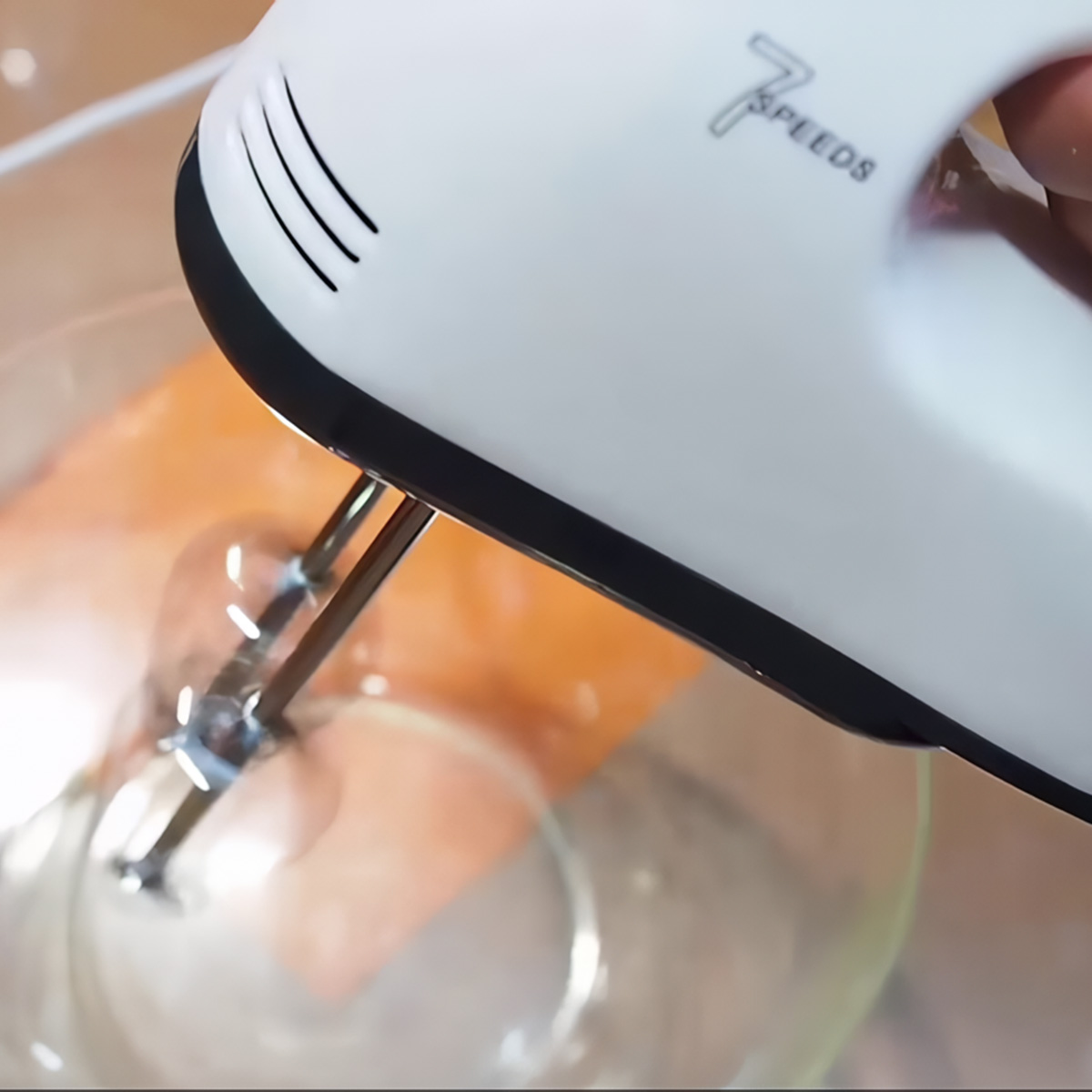 Sbattitore elettrico bianco con fruste cromate, mescola in una ciotola trasparente.