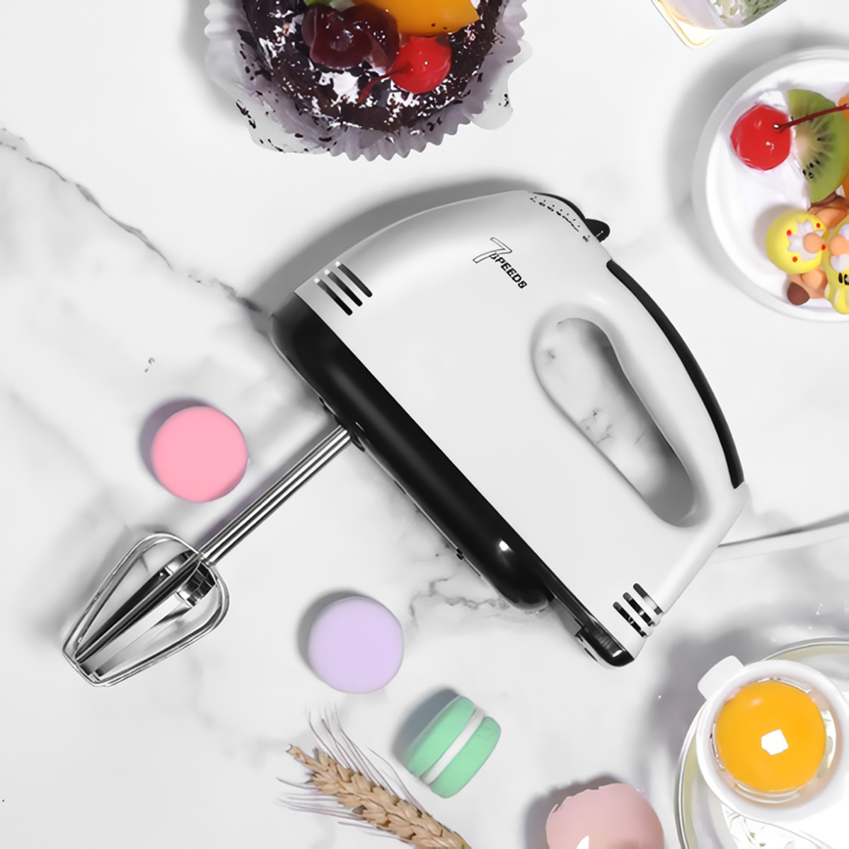 Un frullatore a mano bianco con accenti neri, circondato da macaron e torta.