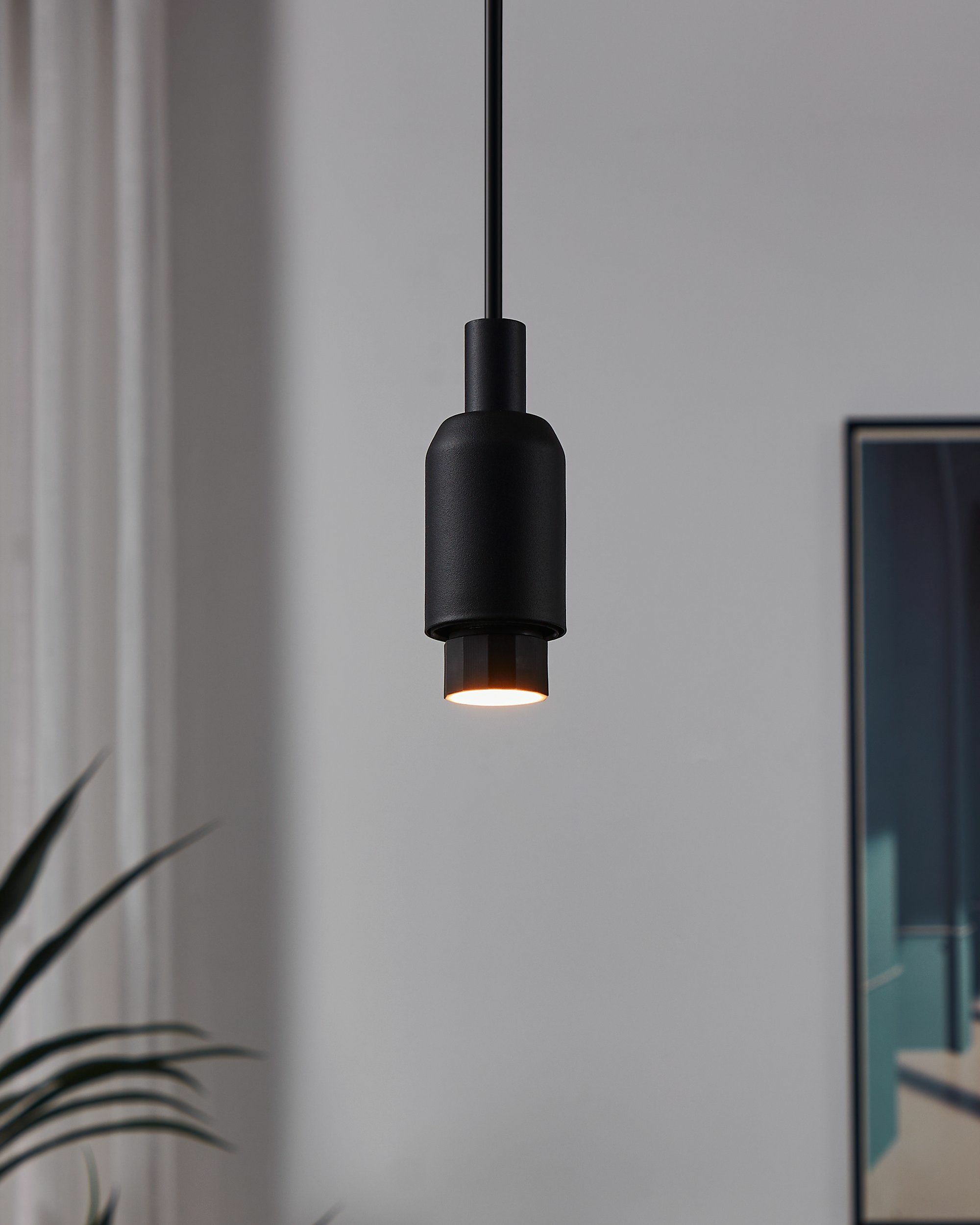 Una lampada a sospensione nera emette una luce calda.