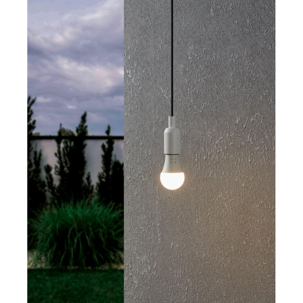 Una lampadina LED bianca pende da un cavo nero contro un muro grigio testurizzato.