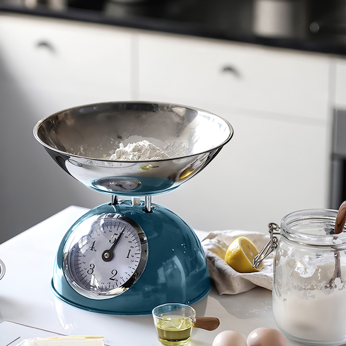 Una báscula de cocina azul verdoso con harina en el bol, junto a huevos, limón y azúcar.