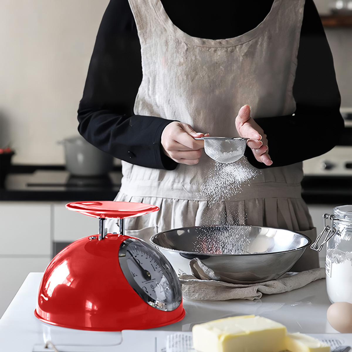 Una persona cierne azúcar glas en un bol, una báscula de cocina roja está cerca.