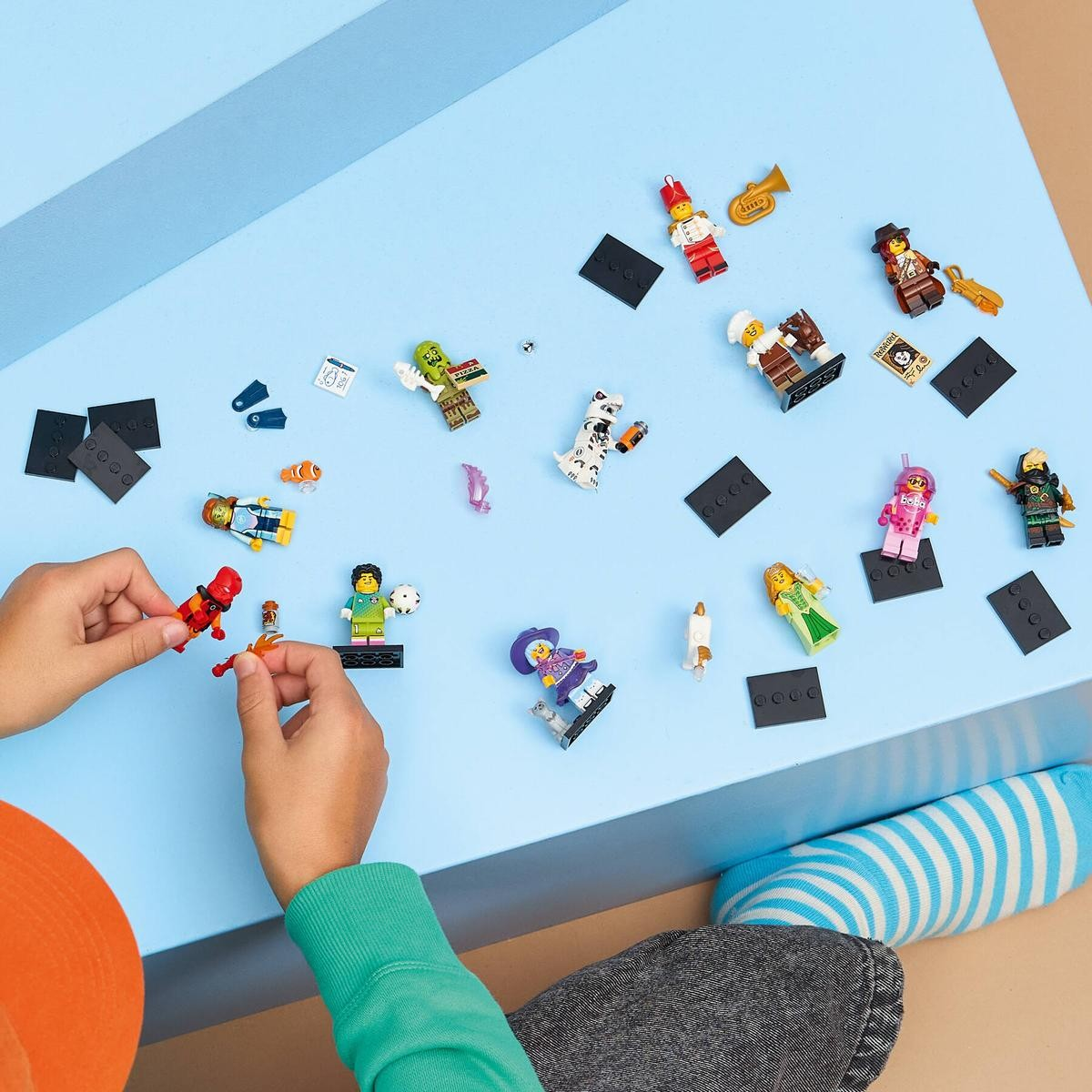 Mani giocano con personaggi Lego: cane, pizzaiolo, ragazza, soldato, musicista.