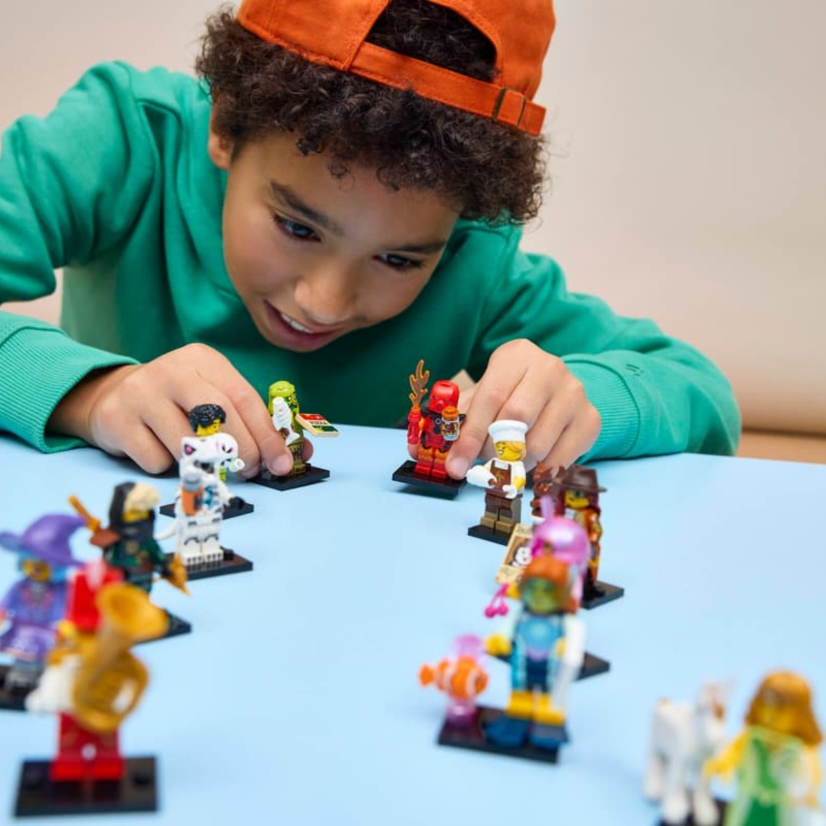 Un ragazzo gioca con le action figure Lego su un tavolo blu.