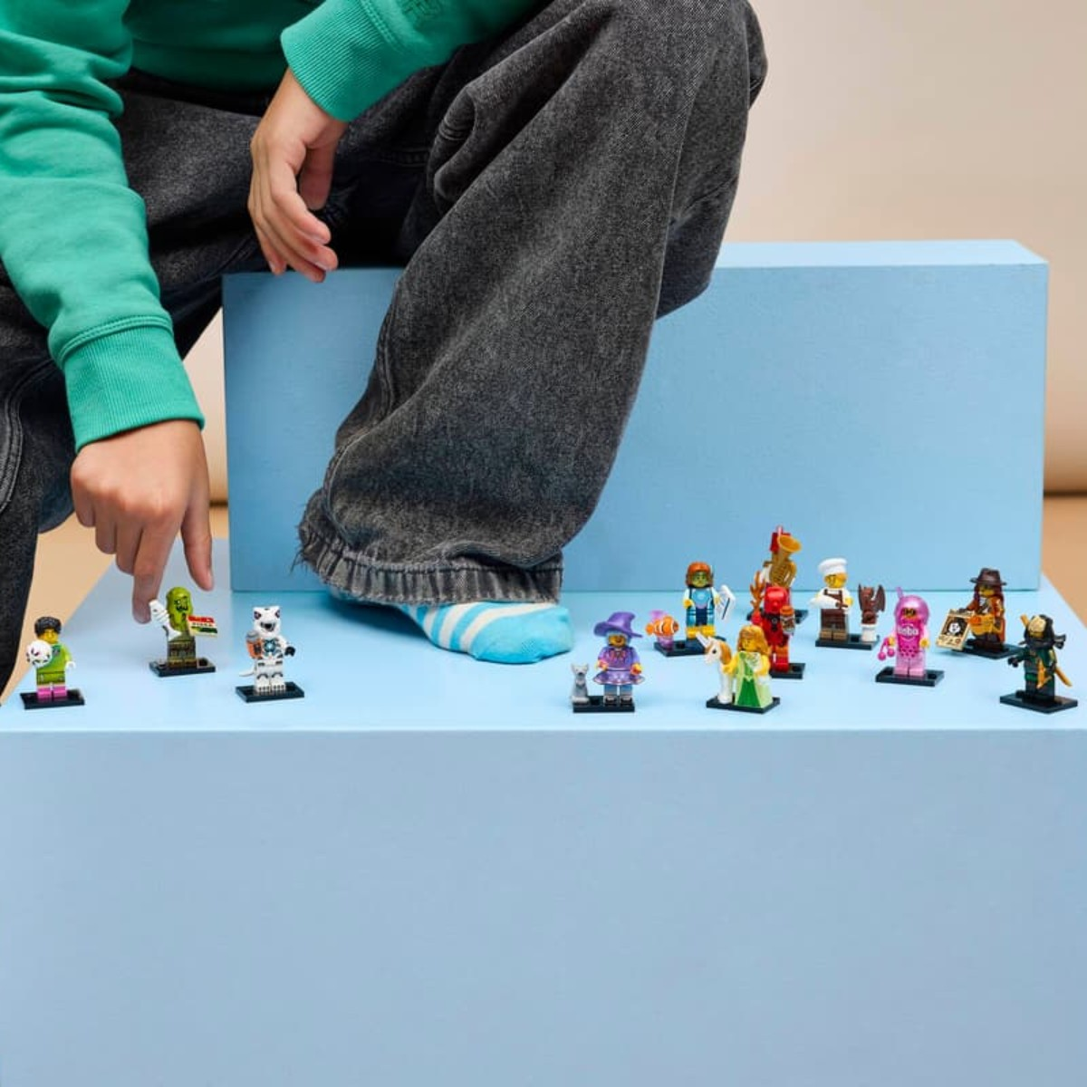 Un bambino con maniche verdi indica una fila di minifigure Lego su una piattaforma blu.