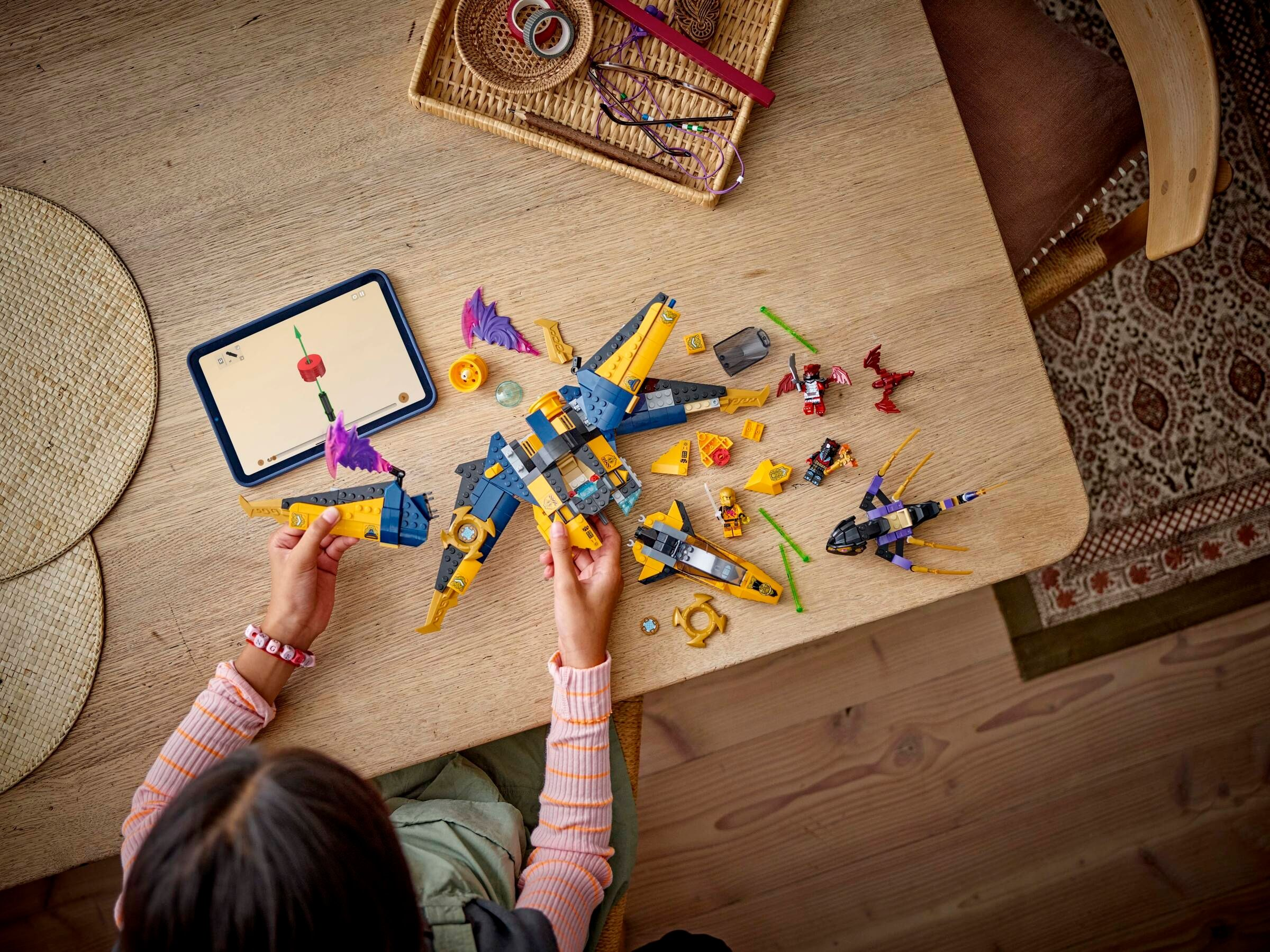 Kind baut gelbes und blaues Lego-Raumschiff mit Tablet-Anleitung auf Holztisch.