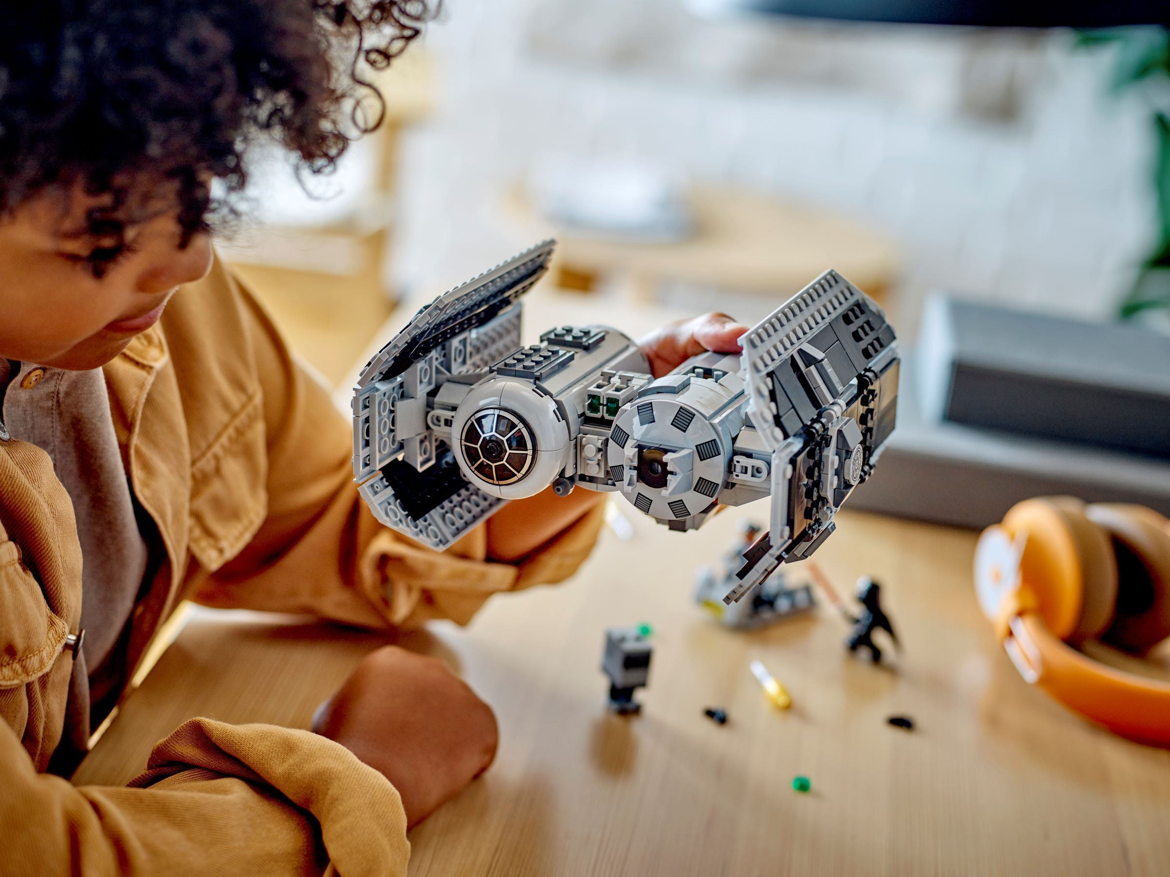 Ein Kind baut ein graues Lego-Raumschiff. Kleine Figuren und Kopfhörer liegen daneben.