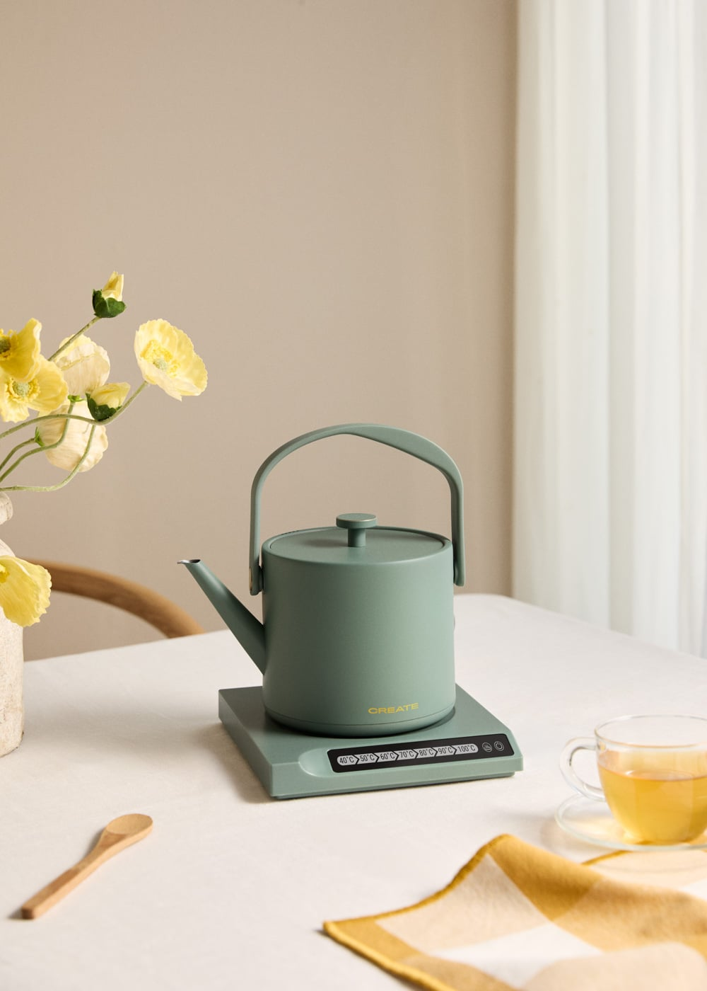 Un hervidor verde sobre una base con ajustes de temperatura. Al lado, un vaso de té.