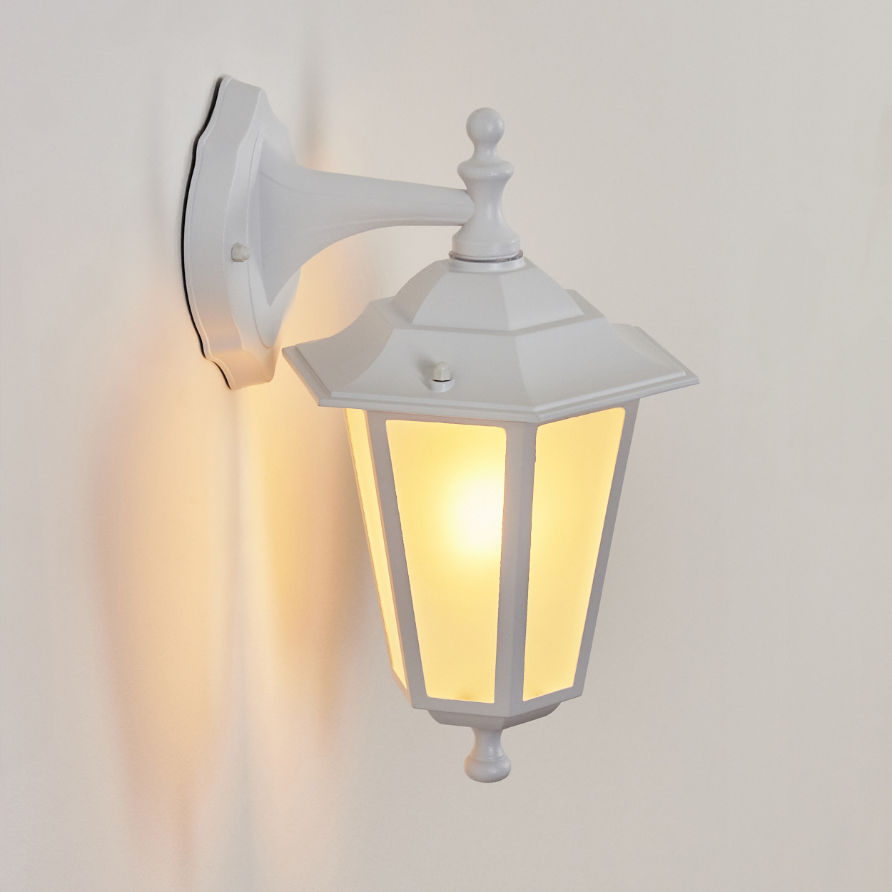 Eine weiße Wandleuchte mit gelbem Licht leuchtet an einer cremefarbenen Wand.