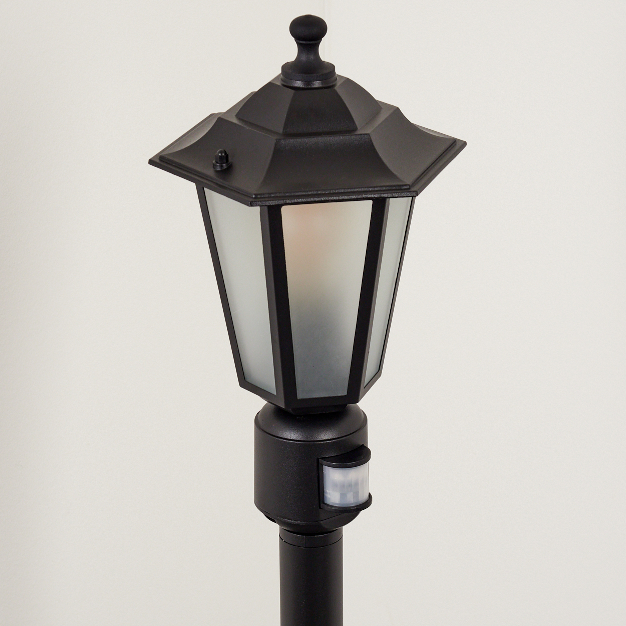 Eine schwarze Außenlampe mit Bewegungsmelder auf grauem Hintergrund.