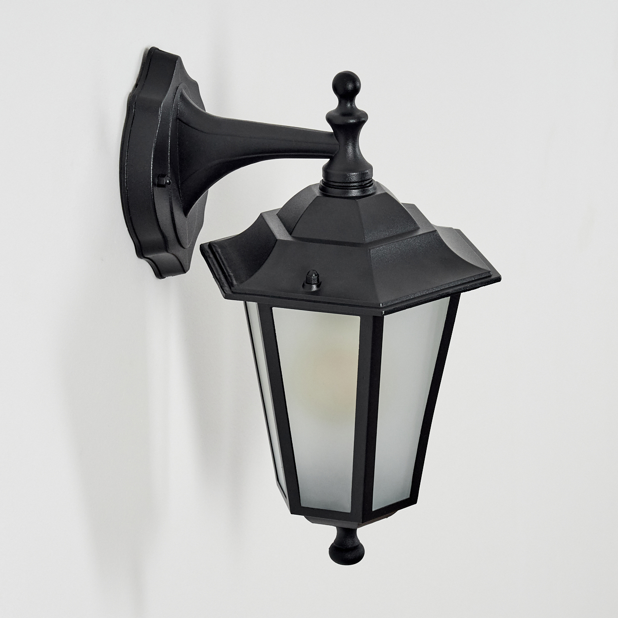 Eine schwarze Wandlampe mit sechseckigem Lampenschirm und Milchglas.
