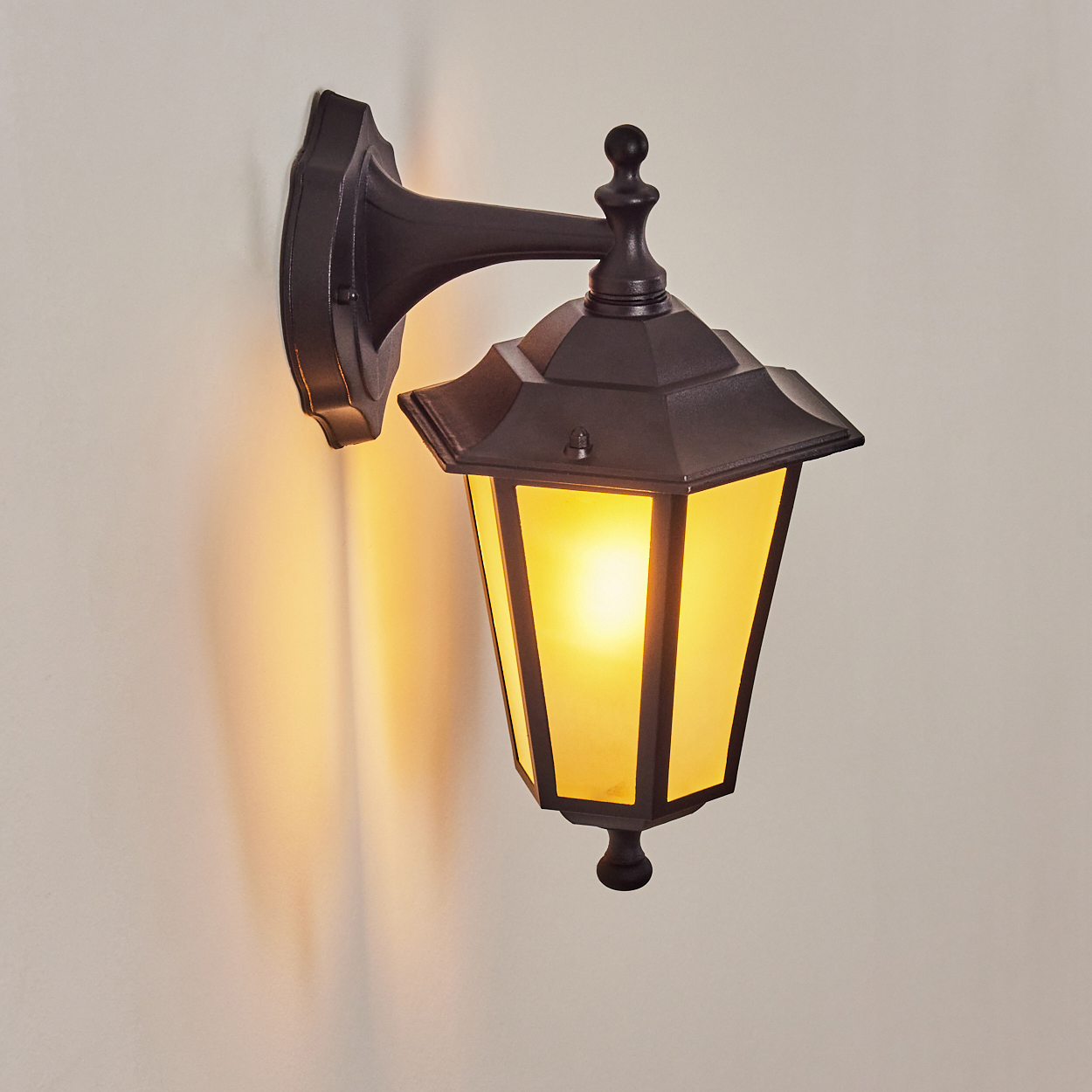 Eine dunkle Wandlaterne mit gelbem Licht leuchtet an einer weißen Wand.