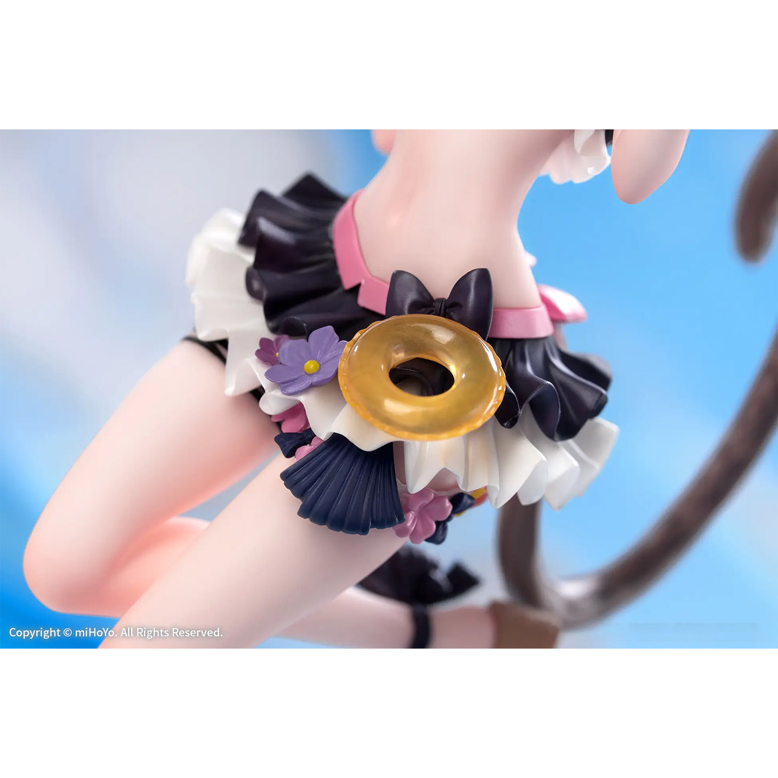 Figurdetail: Ein goldener Donut mit lila Blumen auf einem Rüschenrock.