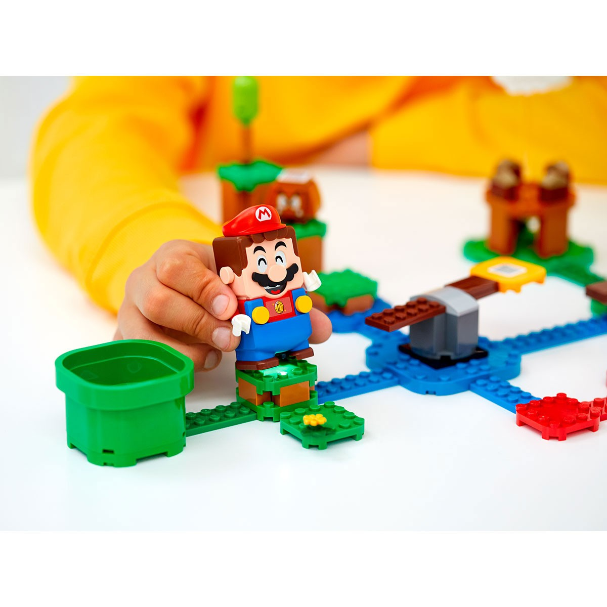 Un bambino gioca con una figura Lego di Mario e un tubo verde su un tavolo bianco.