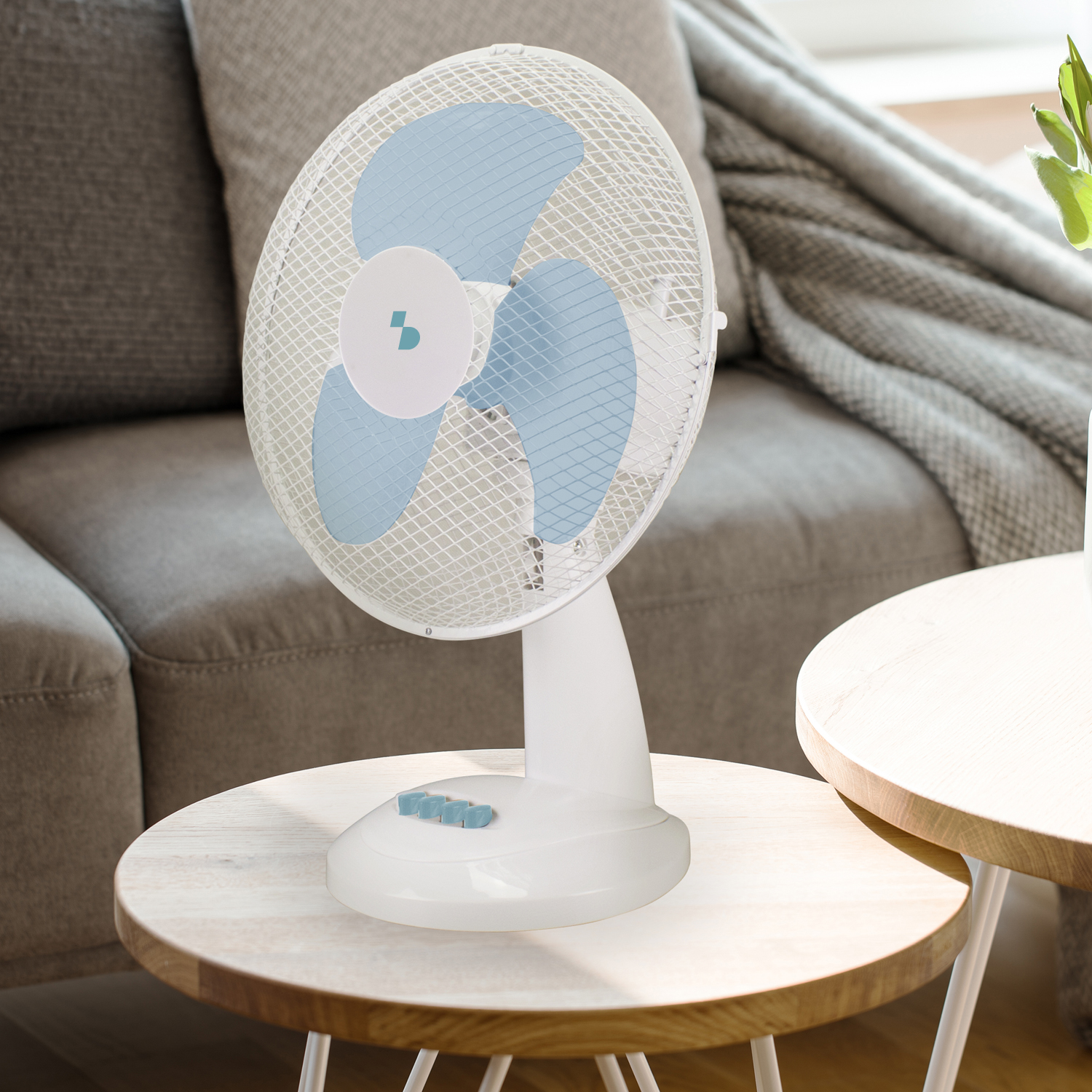 Un ventilatore da tavolo bianco con pale blu è su un tavolino di legno.