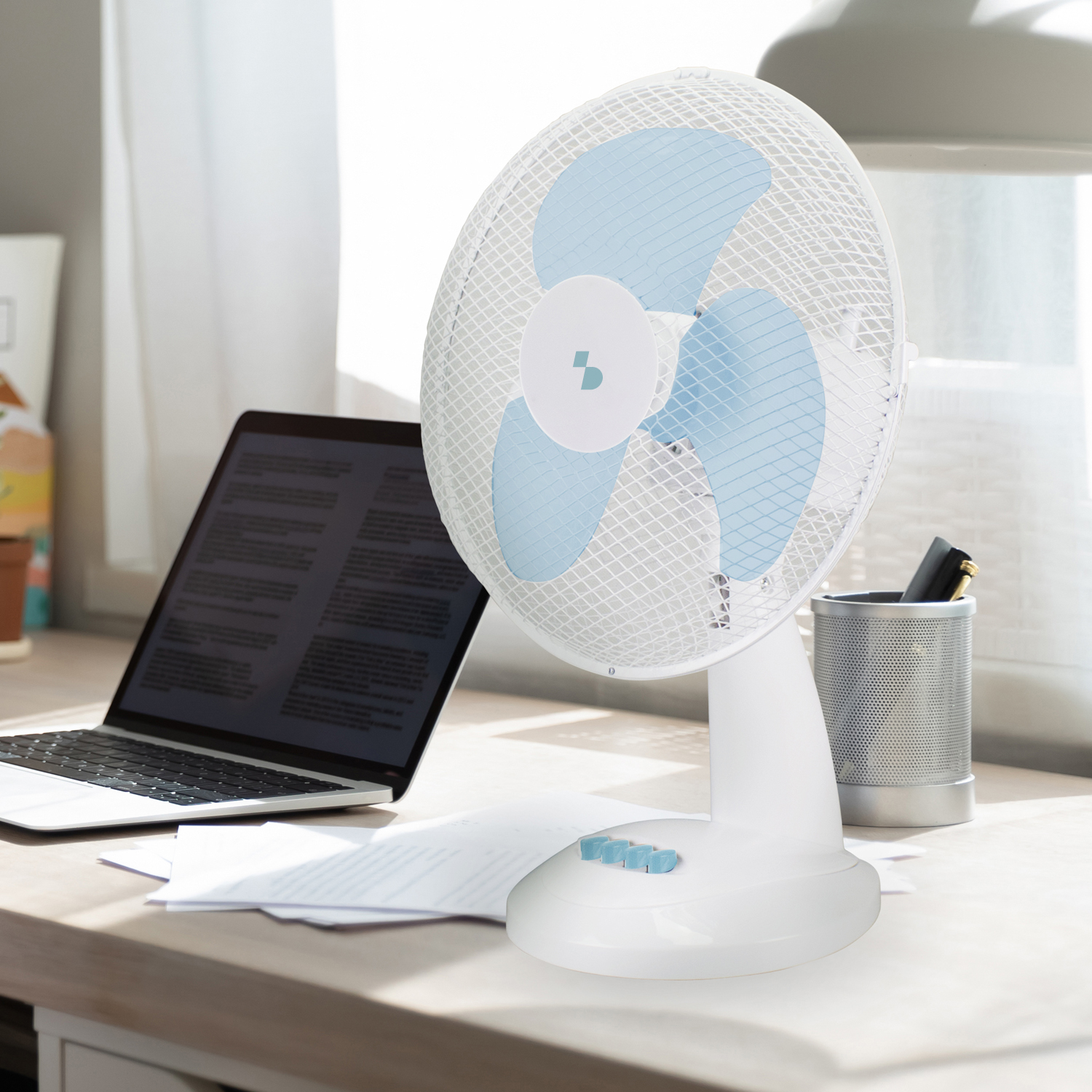 Un ventilatore da scrivania bianco con pale blu è su una scrivania di legno accanto a un laptop.