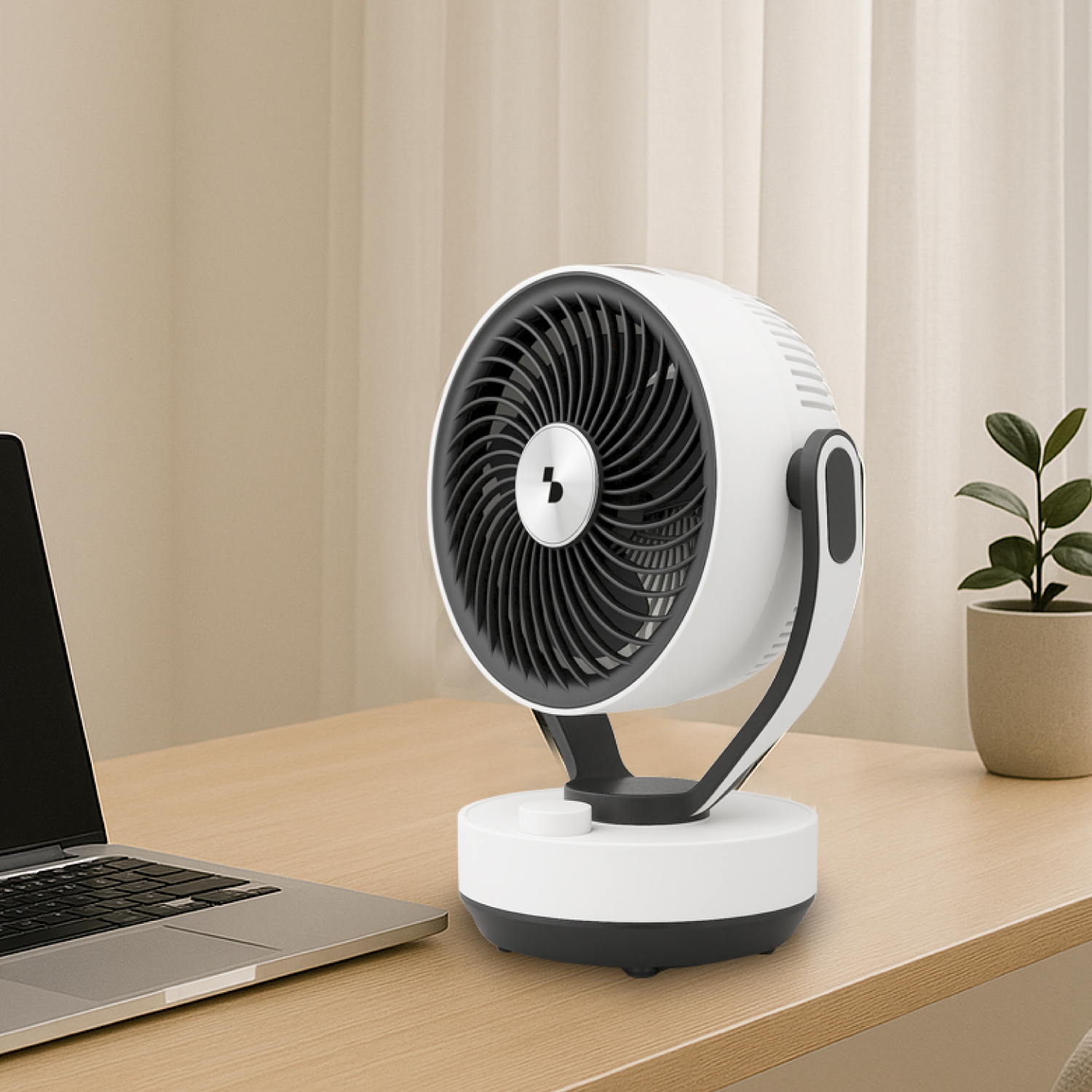 Un ventilatore da scrivania bianco con griglia nera si trova su una scrivania di legno accanto a un laptop e una pianta.