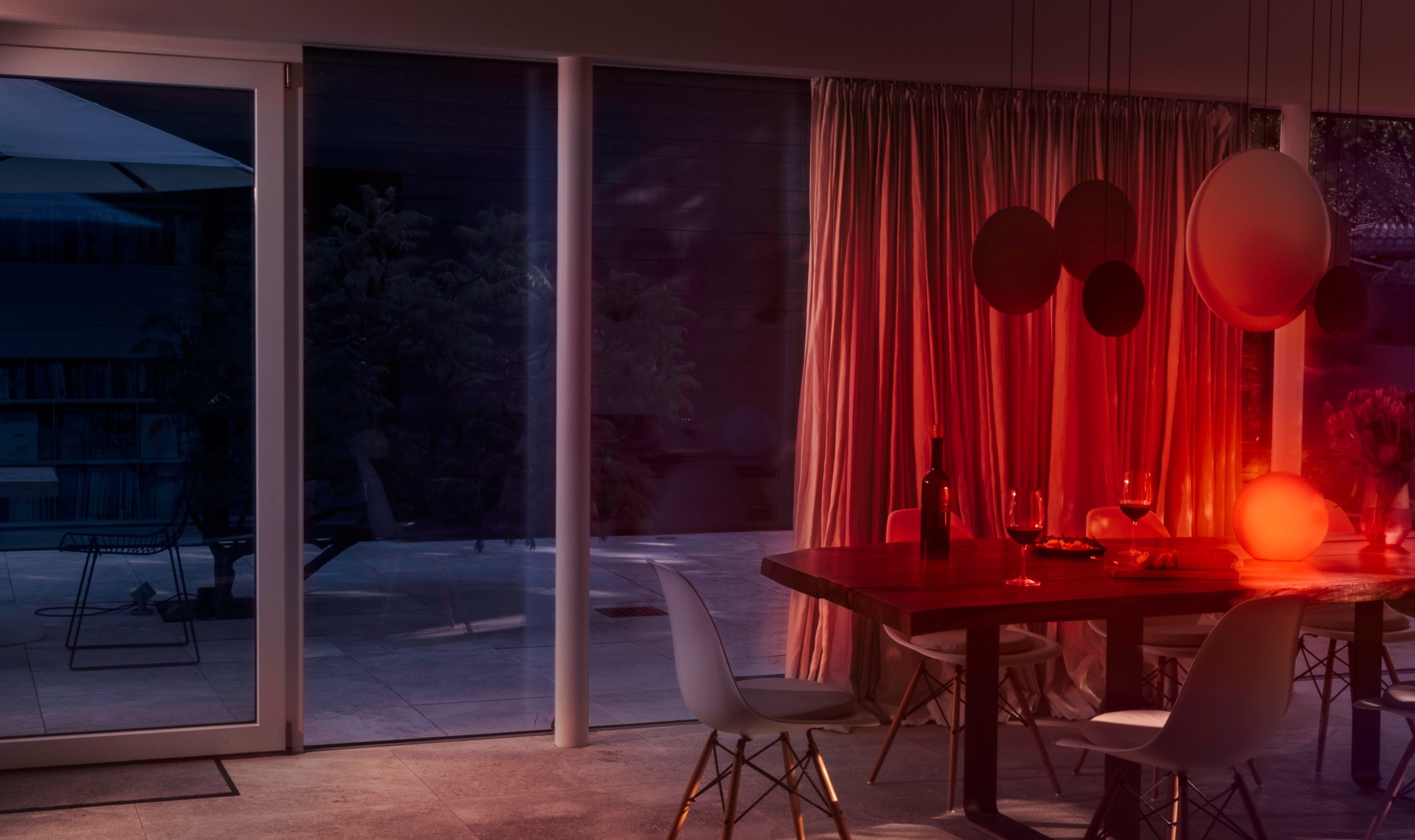 Une table de salle à manger avec des verres à vin et une bouteille est éclairée en rouge.