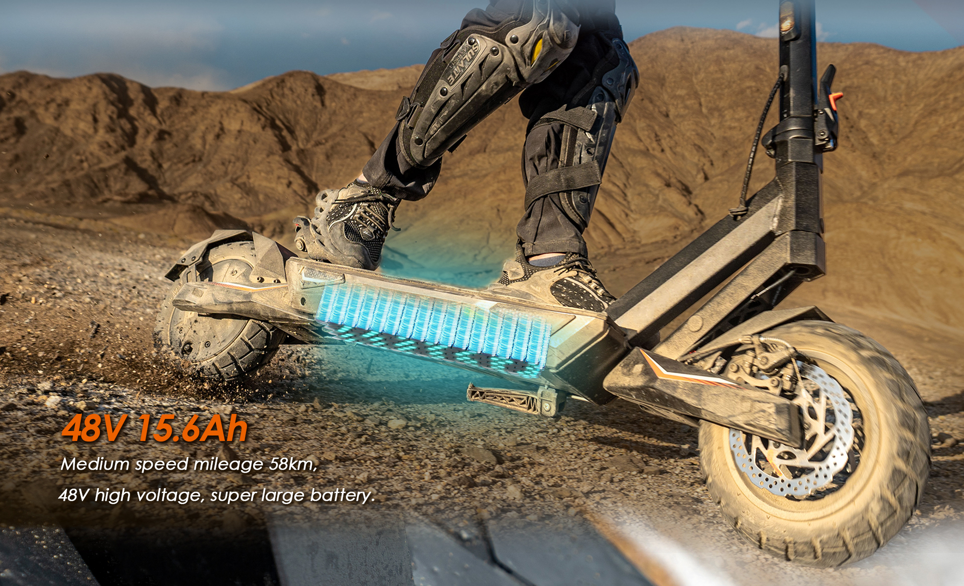 Persona su monopattino elettrico su terreno accidentato, batteria visibile, montagne sullo sfondo.