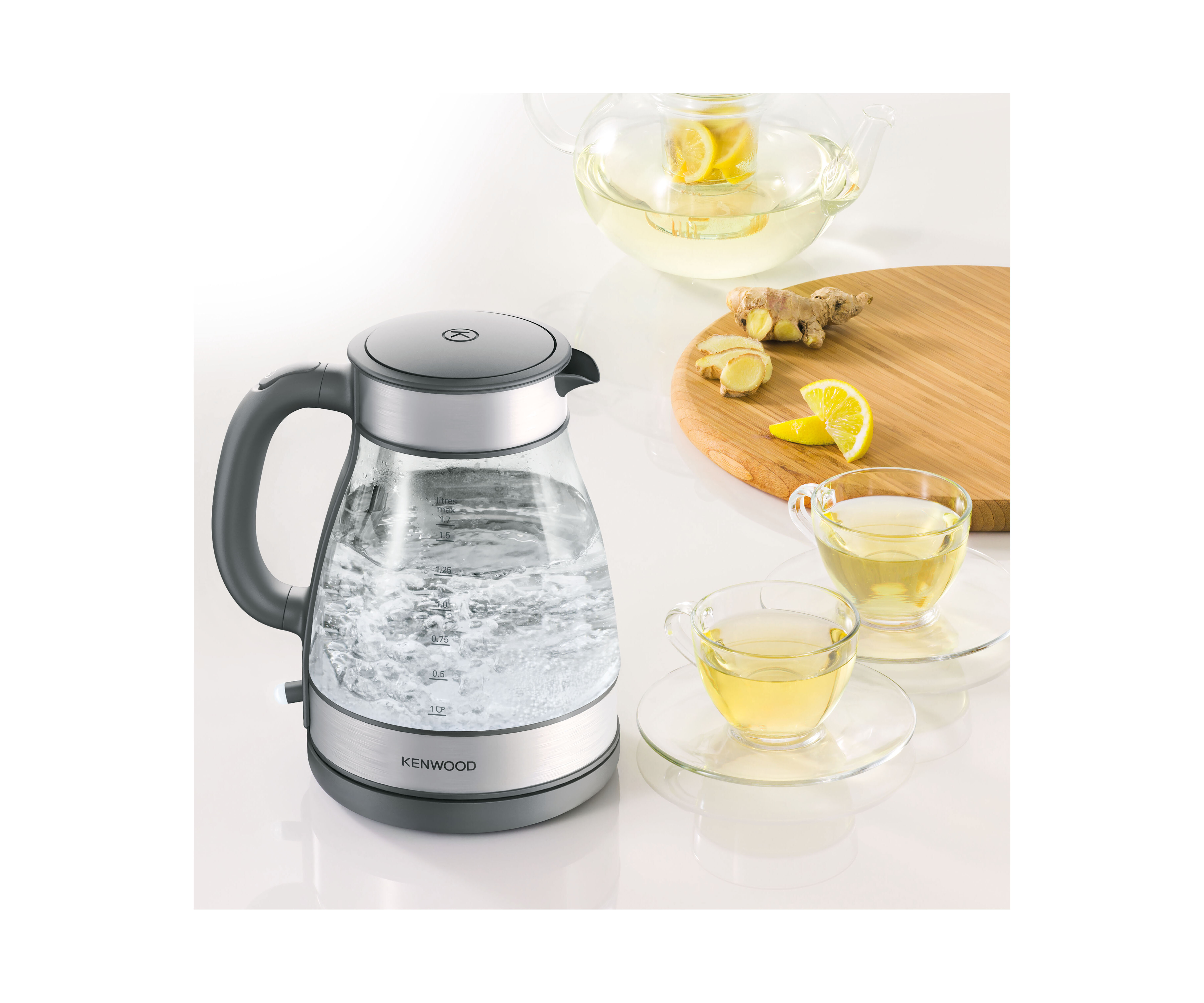 Ein Wasserkocher mit kochendem Wasser neben zwei Tassen Tee mit Zitrone und Ingwer.